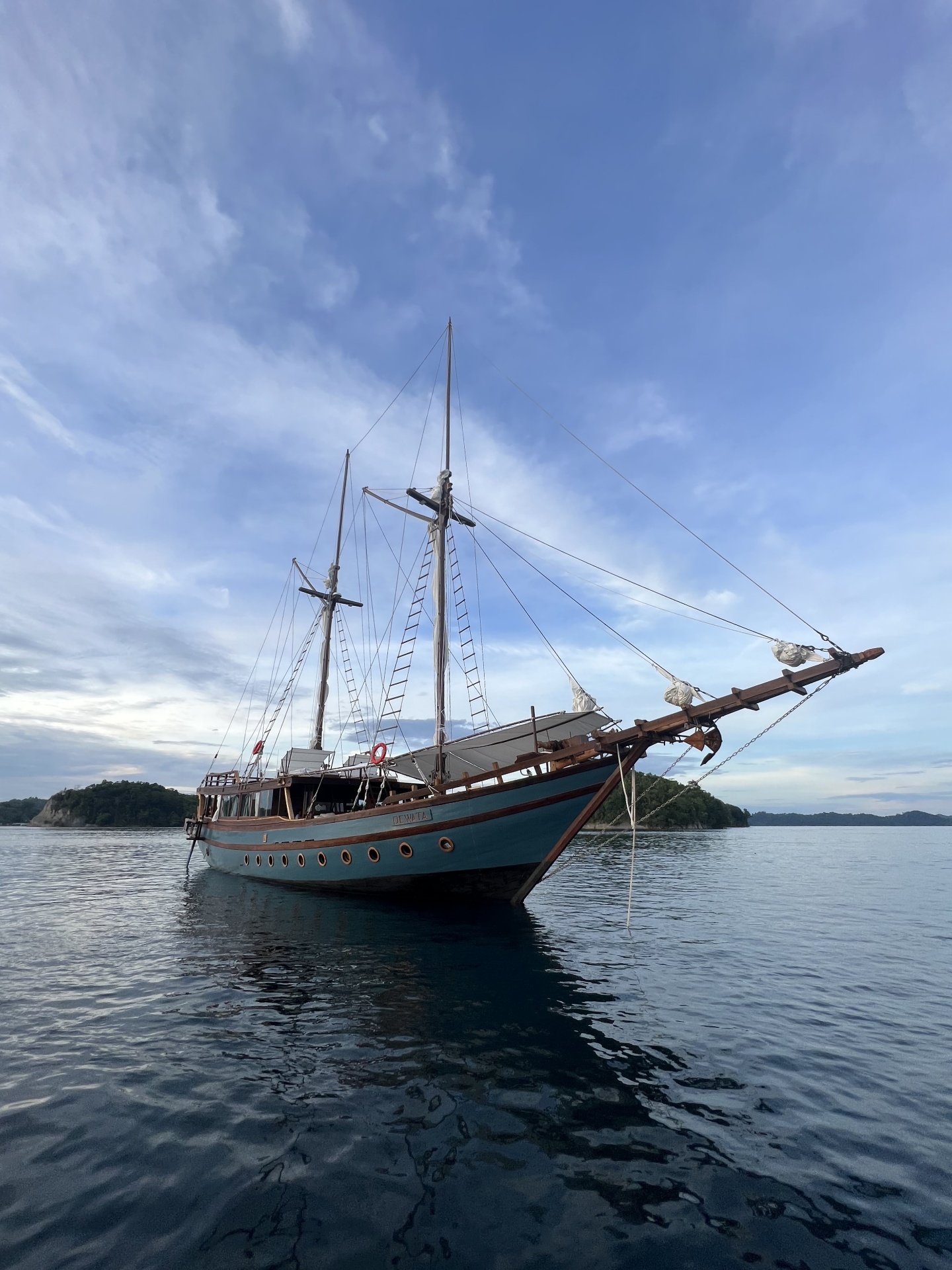 Dewata phinisi at anchor in a calm Raja Ampat bay at sunset with pastel sky