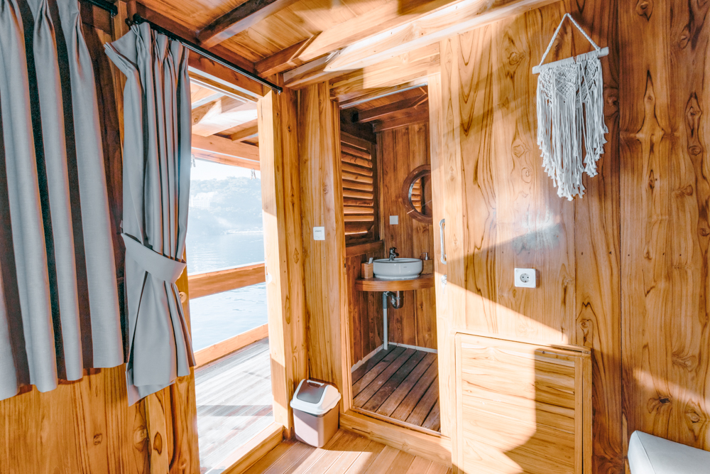 Andamari cabin doorway opening toward the bathroom and exterior deck, with sunlight across the teak interior
