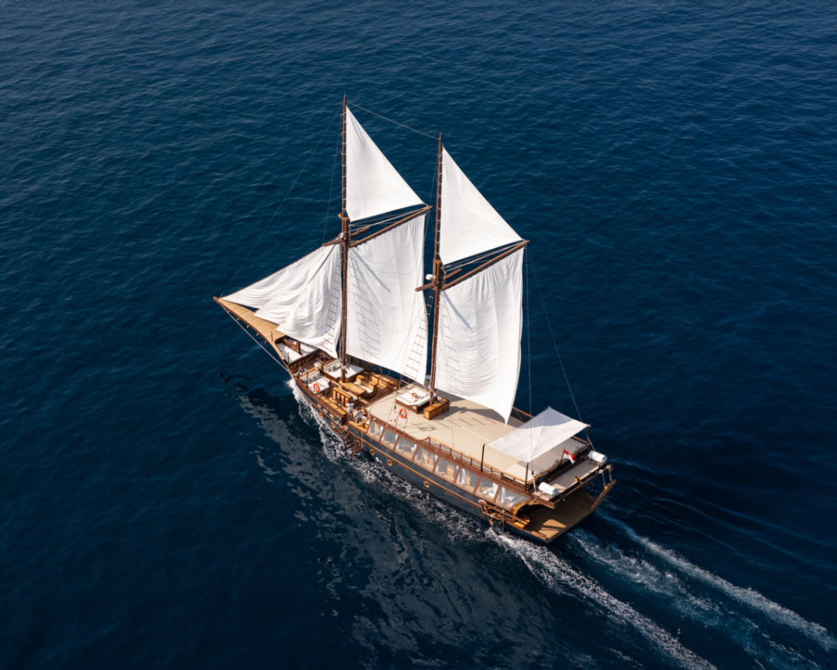Aerial stern-quarter view of Sanya underway with white sails drawing and wake trailing behind