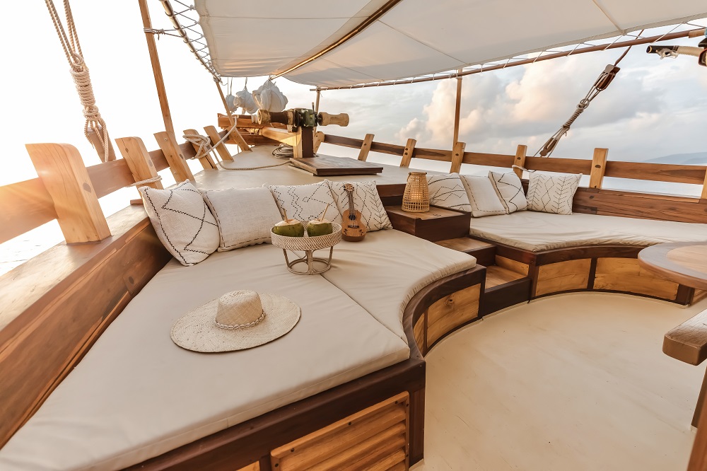 Bow lounge on Senja in daylight with cushions, ukulele, straw hat and fresh coconuts under white sun sails