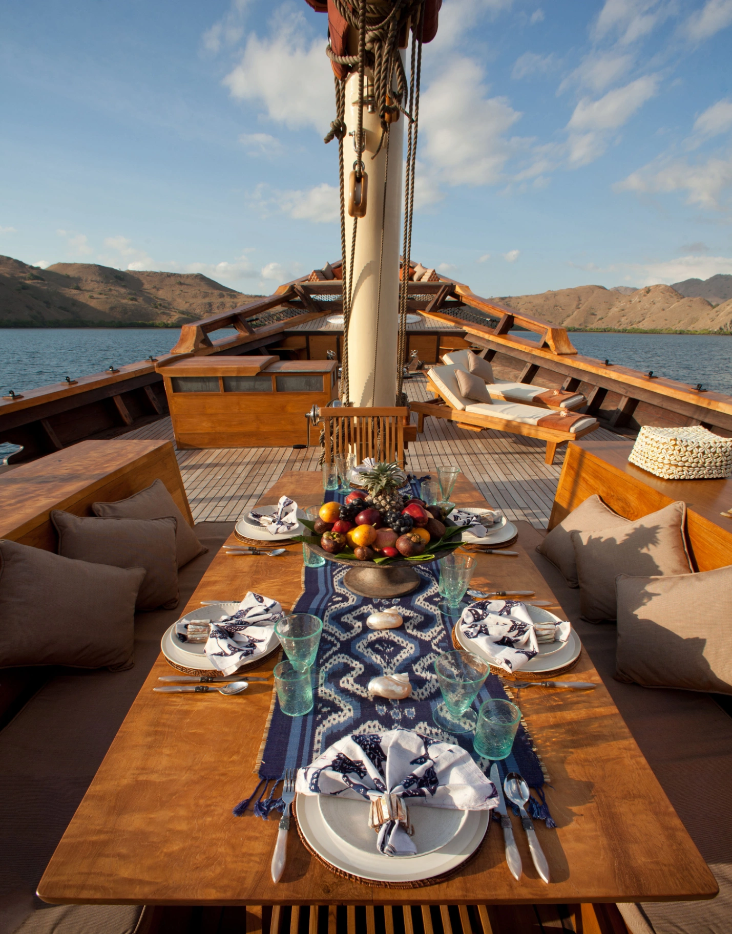 Foredeck dining table set with fresh fruit and ikat runner on Si Datu Bua, mountain backdrop