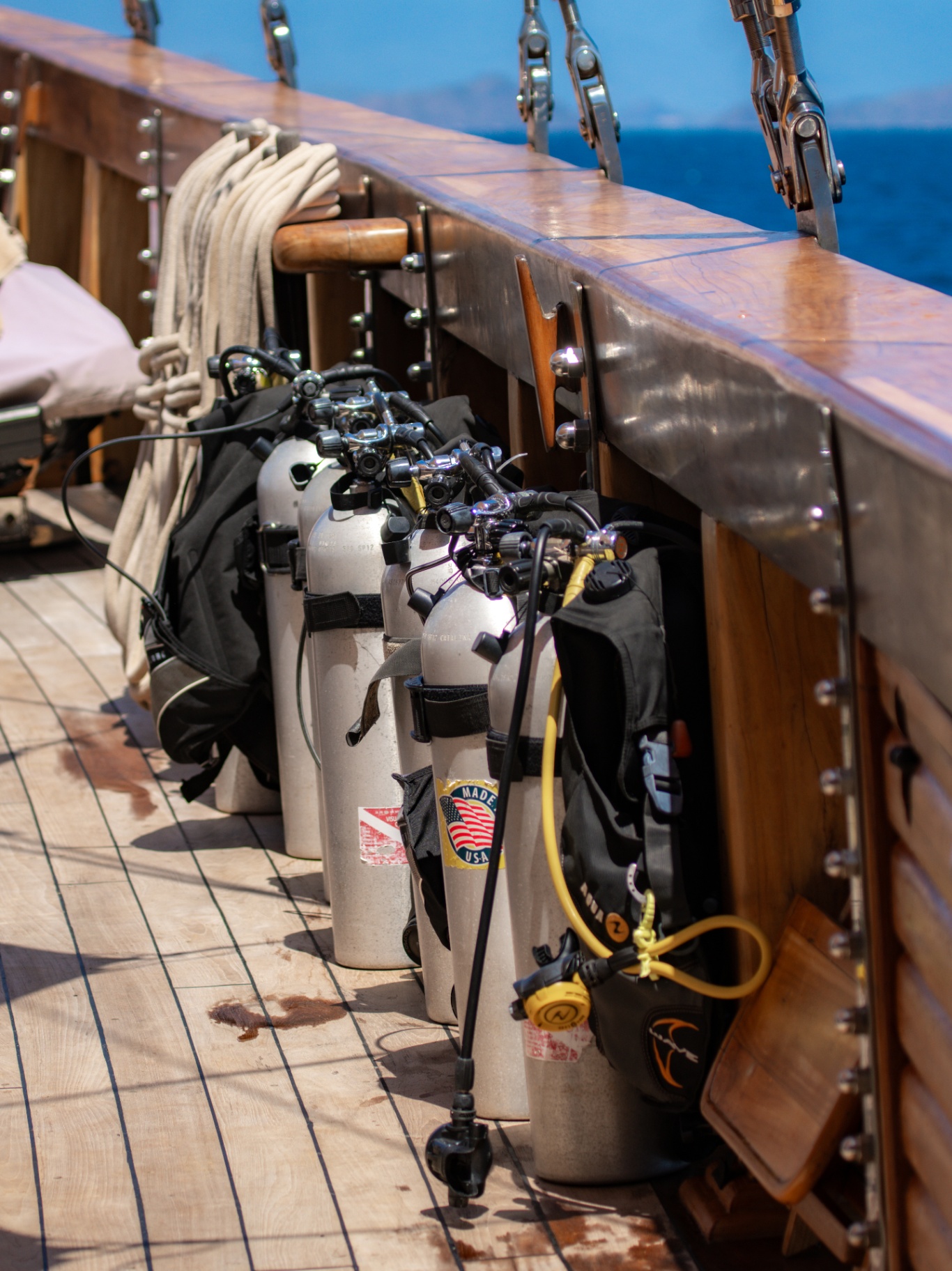 Row of scuba tanks with regulators secured along Lamima's teak deck rail ready for a dive