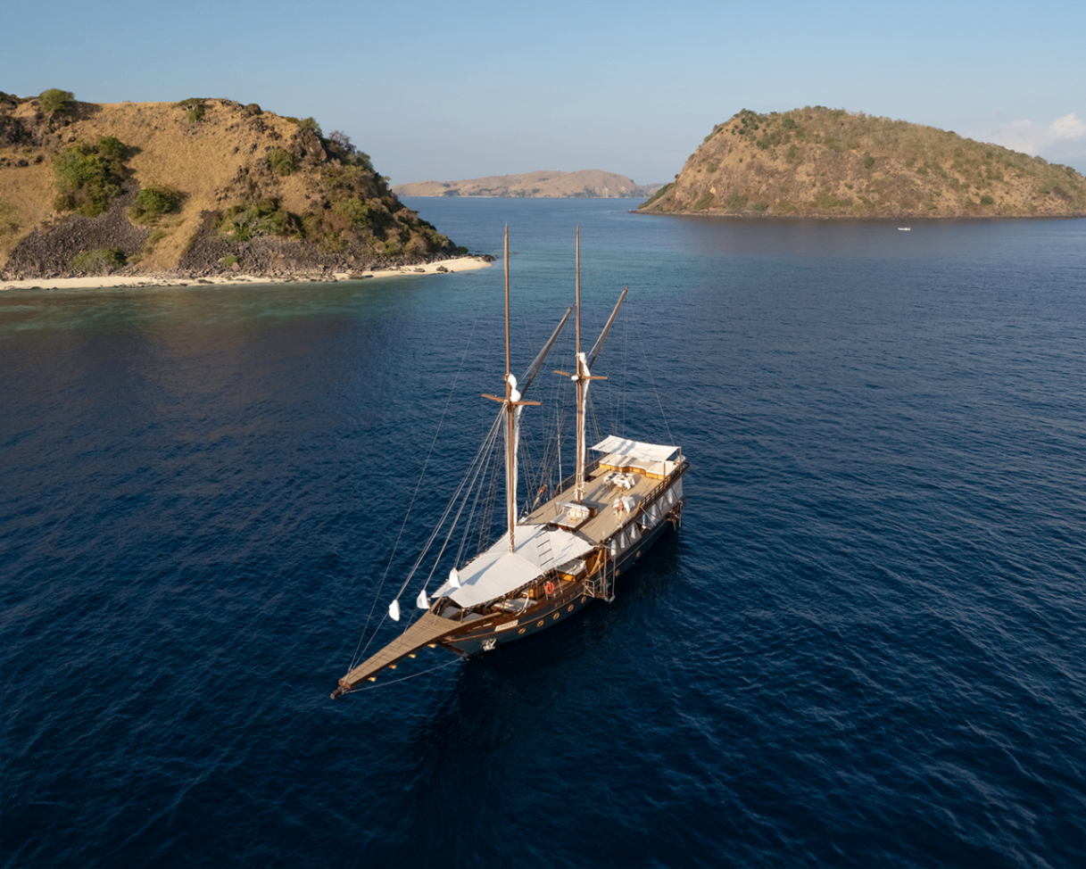 Sanya at anchor in a Komodo channel with dry hills and islands in the distance