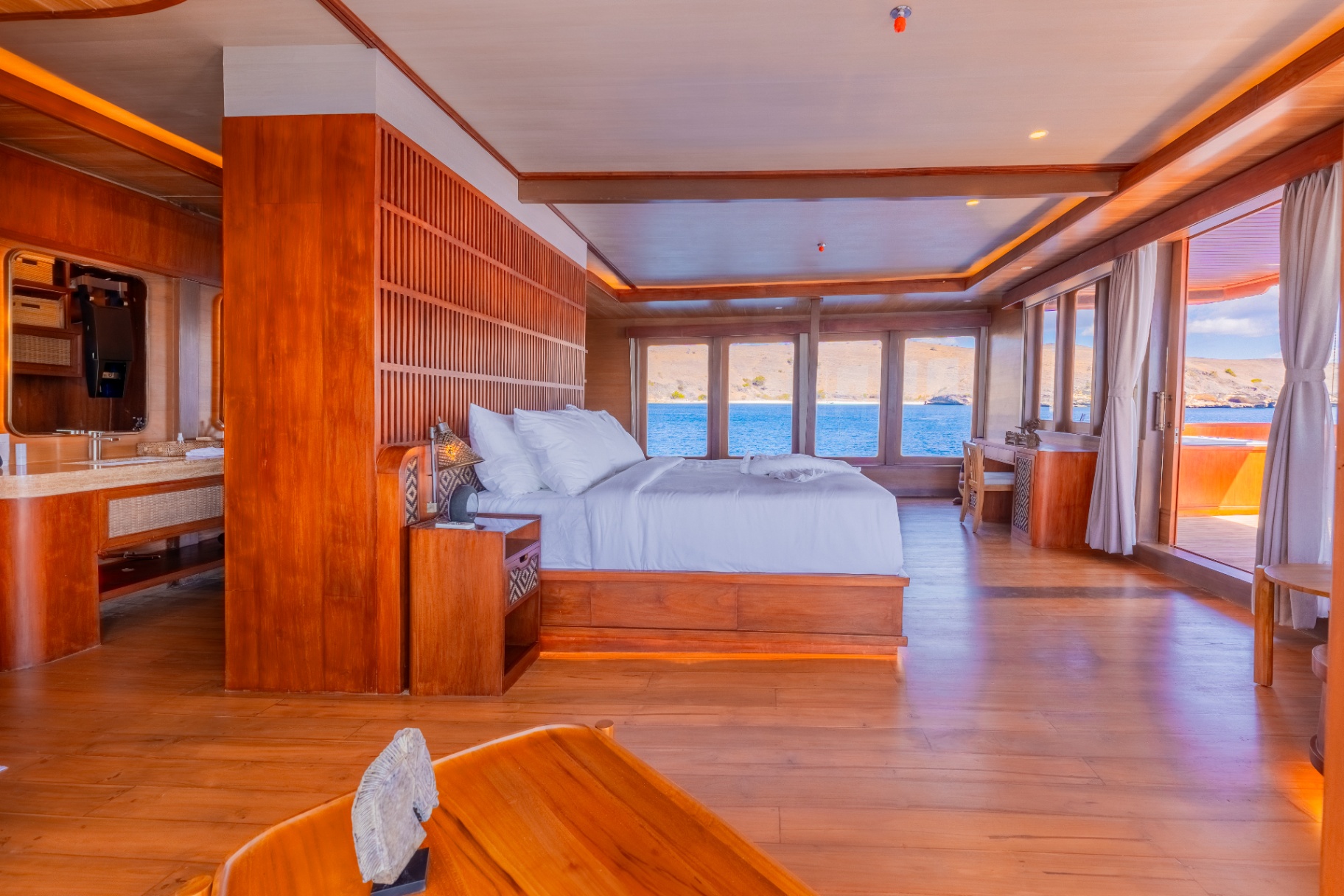 Master cabin on Sanctuary with king bed, warm teak panelling and panoramic windows over the sea