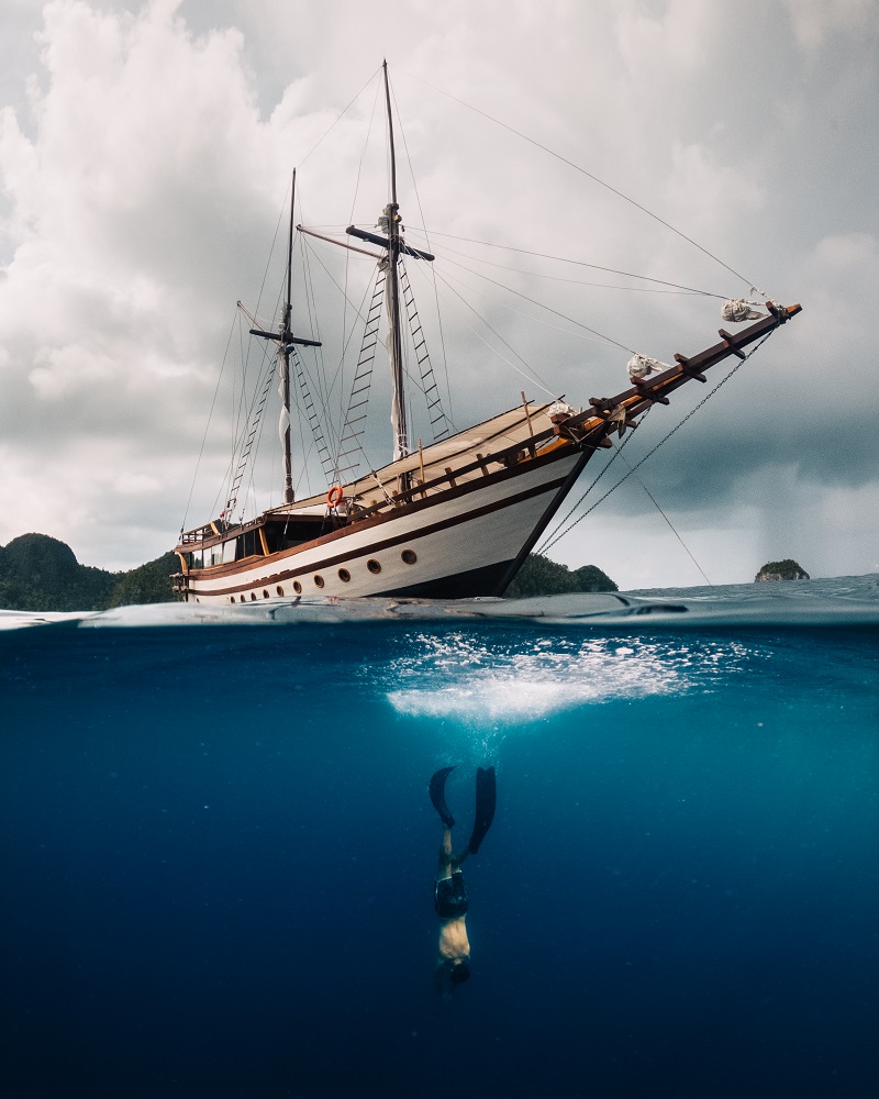 Split-level view of Senja above the water with a freediver descending on a single breath below