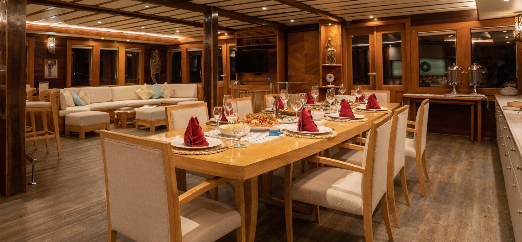Lamima's indoor saloon set for dinner with long teak table, upholstered lounge and warm evening lighting