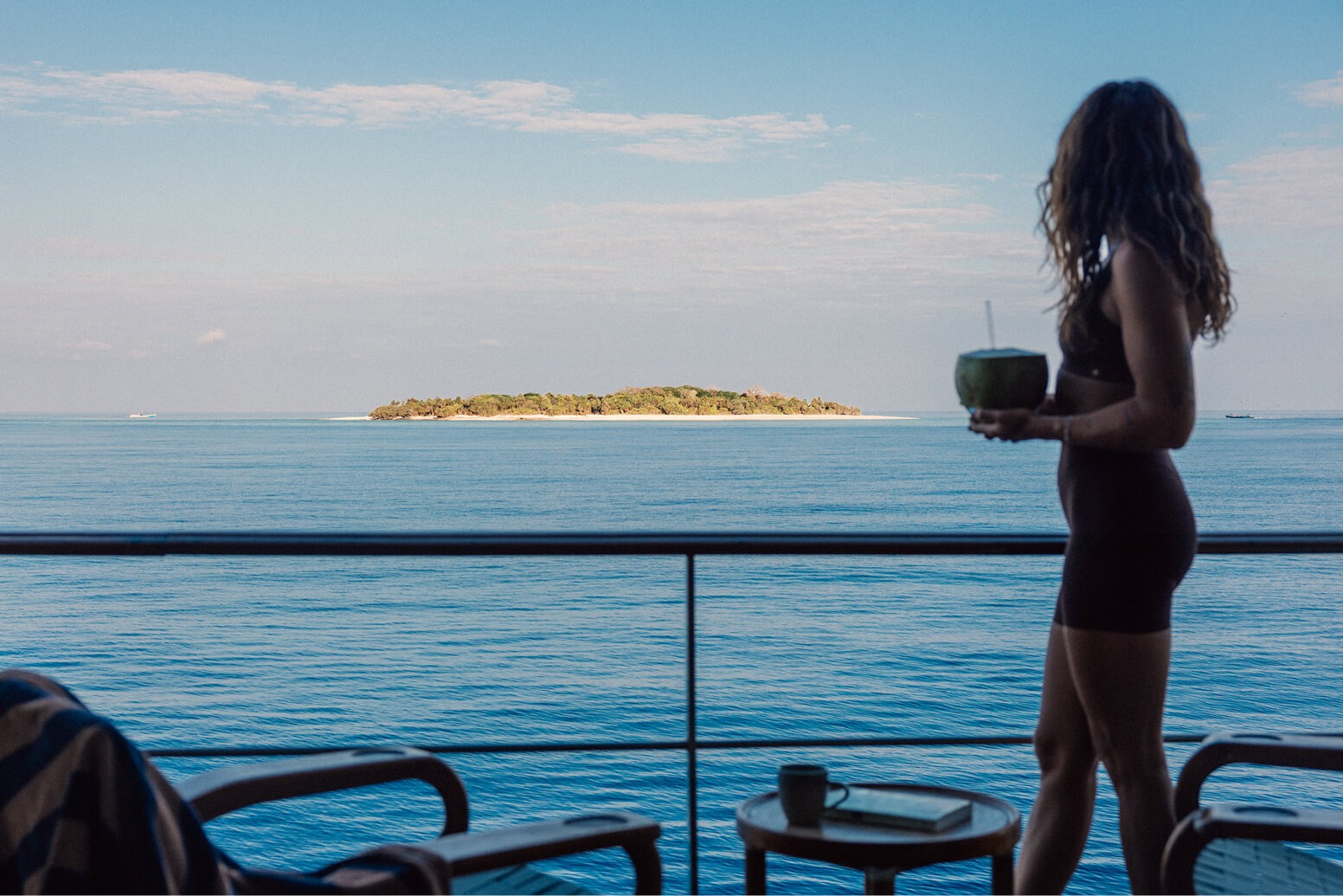Guest with a fresh coconut on the balcony looking at a small island offshore