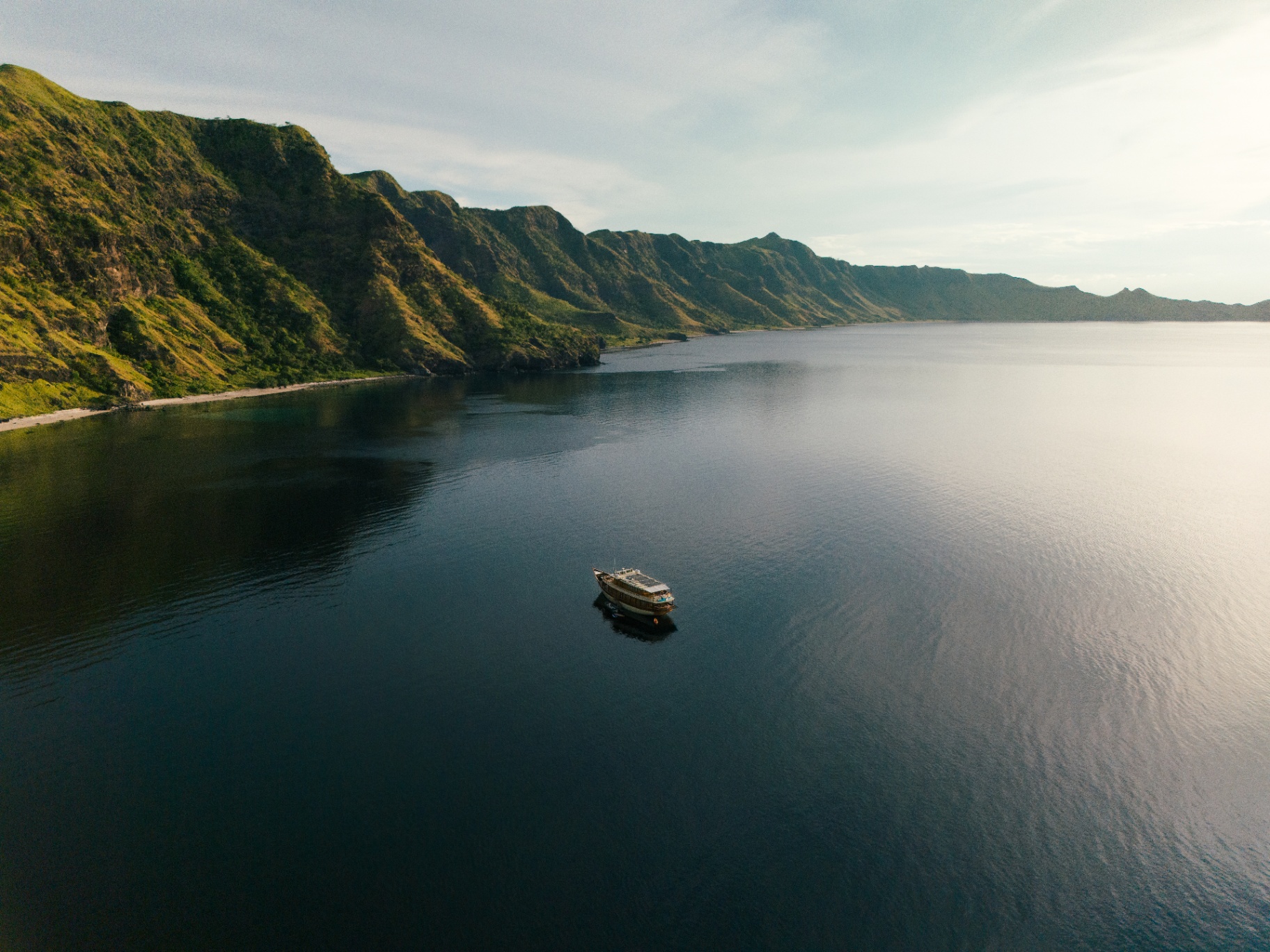 Mischief drifting on inky calm water beneath sunlit Komodo cliffs