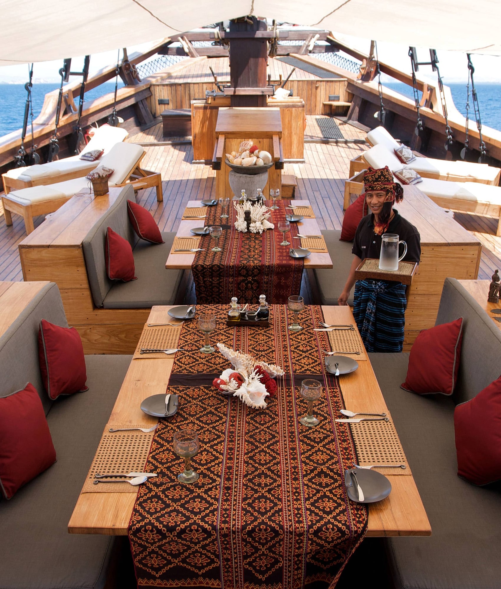Silolona's shaded deck dining area set for lunch with ikat runners and a smiling crew member