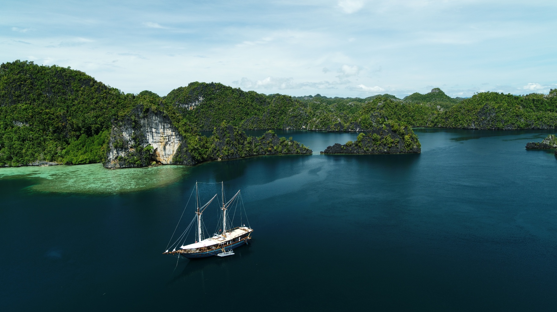 Wide aerial of Dewata anchored in a hidden Raja Ampat lagoon