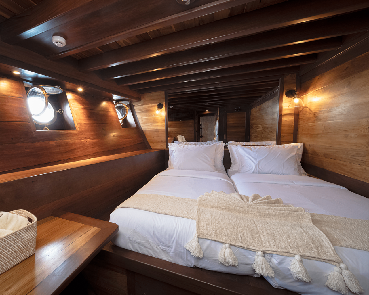 Sanya double guest cabin with cream linens, portholes and glowing wall sconces