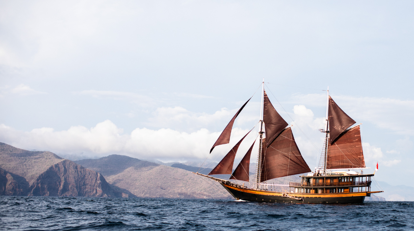 Dunia Baru phinisi under full sail off a mountainous Indonesian coastline