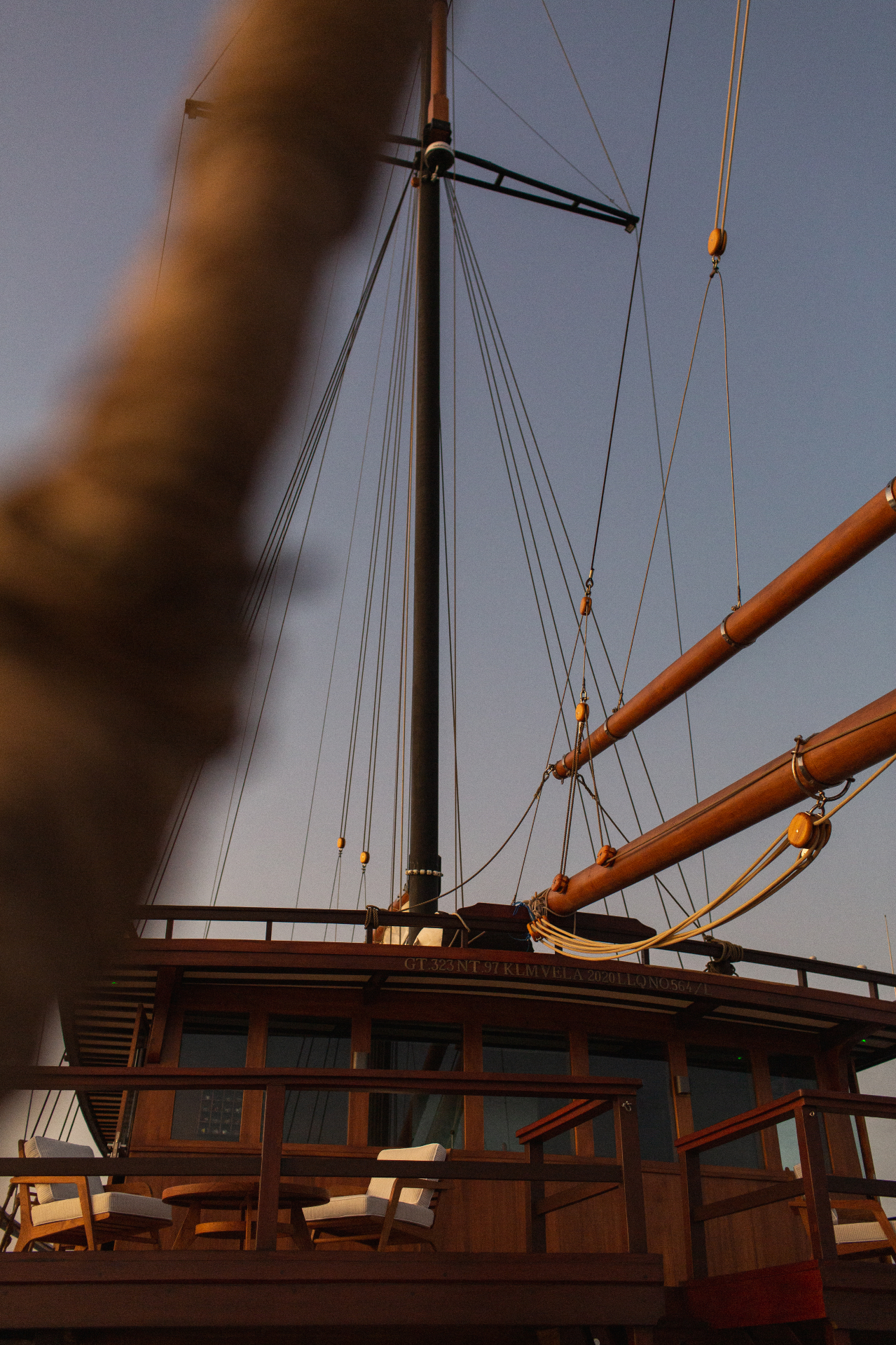 Looking up Vela's mast and rigging from the deck at dusk with the yacht's registration engraved on the wheelhouse