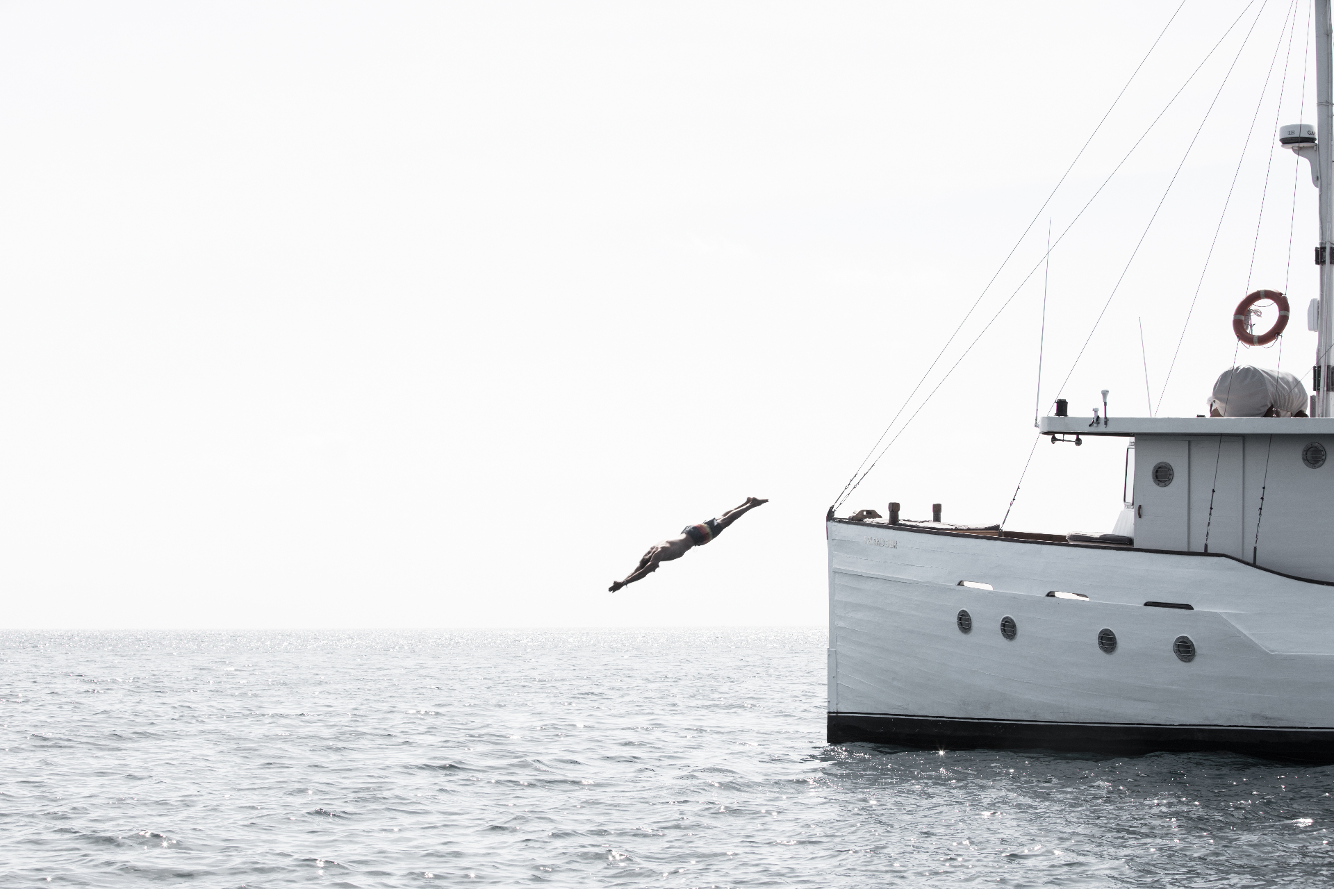 Guest diving from Splendour's bow into calm sea on a bright hazy morning