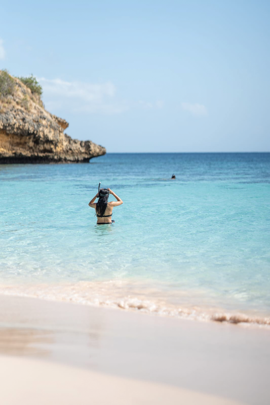 Guest snorkeling from a calm white-sand beach with turquoise water