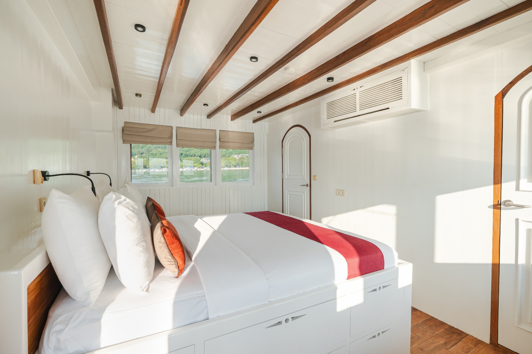 Banda cabin on Mischief with king bed, red throw, exposed wooden beams and sunlit sea-view windows