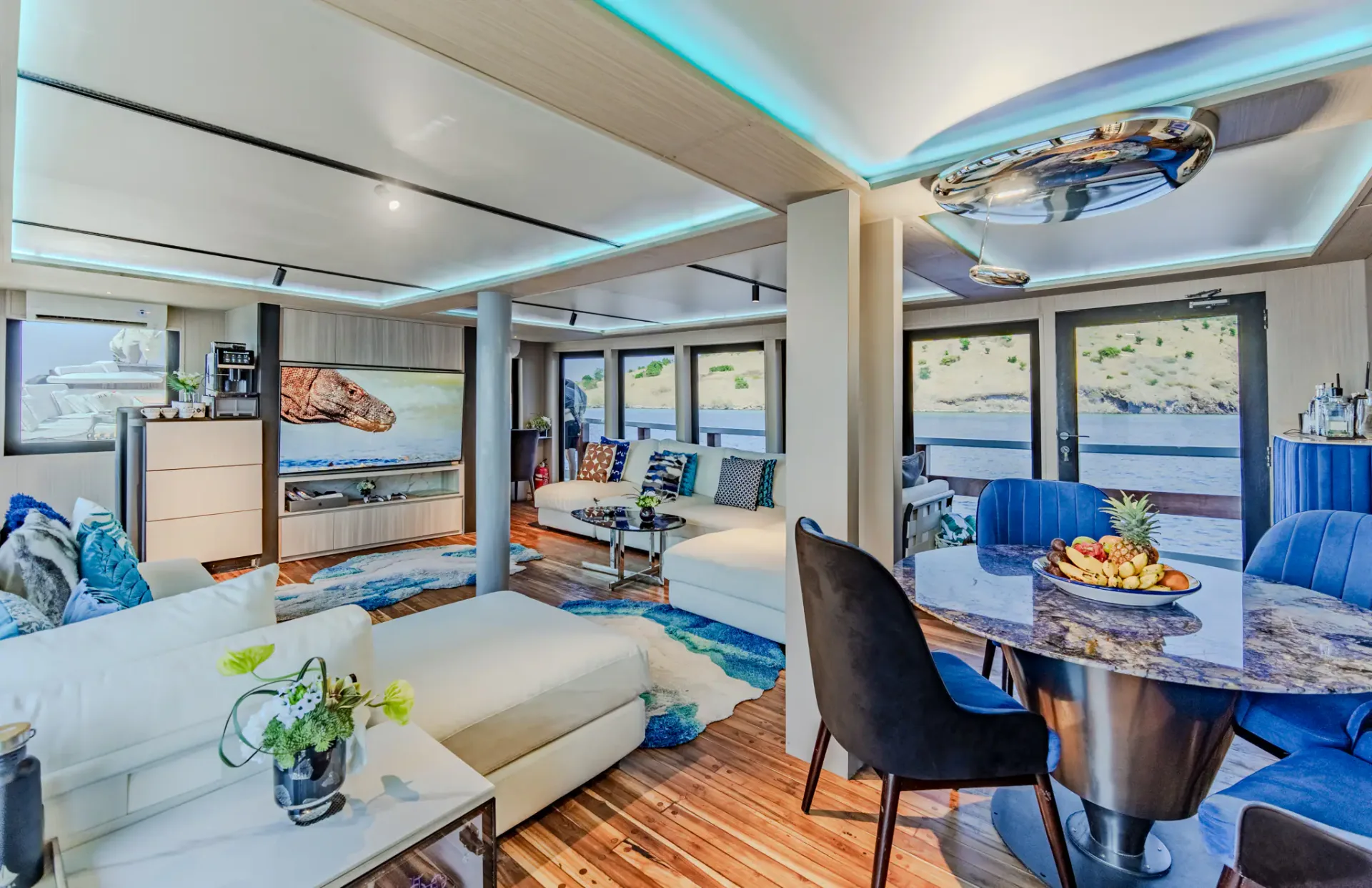 Kayra Phinisi main salon with lounge seating, dining nook and Komodo dragon TV artwork