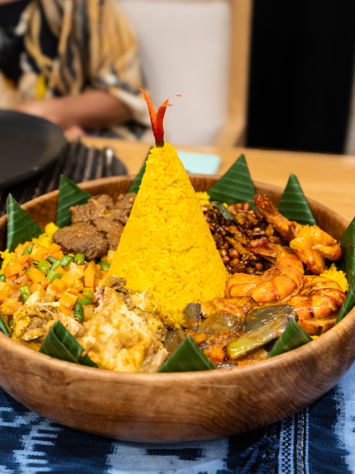 Traditional Indonesian tumpeng — cone of yellow rice with chicken, prawns, beef rendang and vegetables