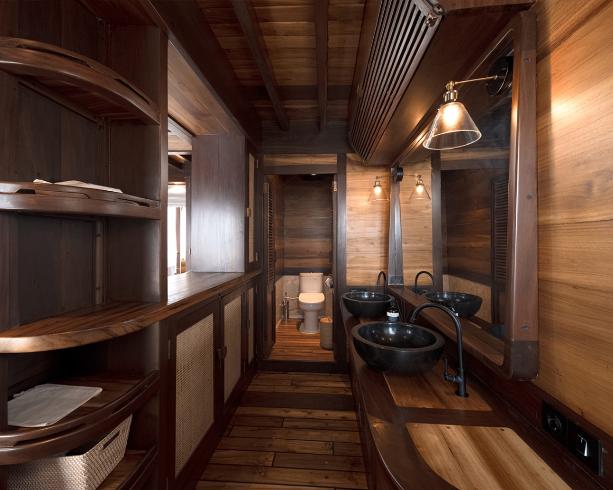 Sanya ensuite bathroom with twin black stone basins, timber shelving and warm lighting