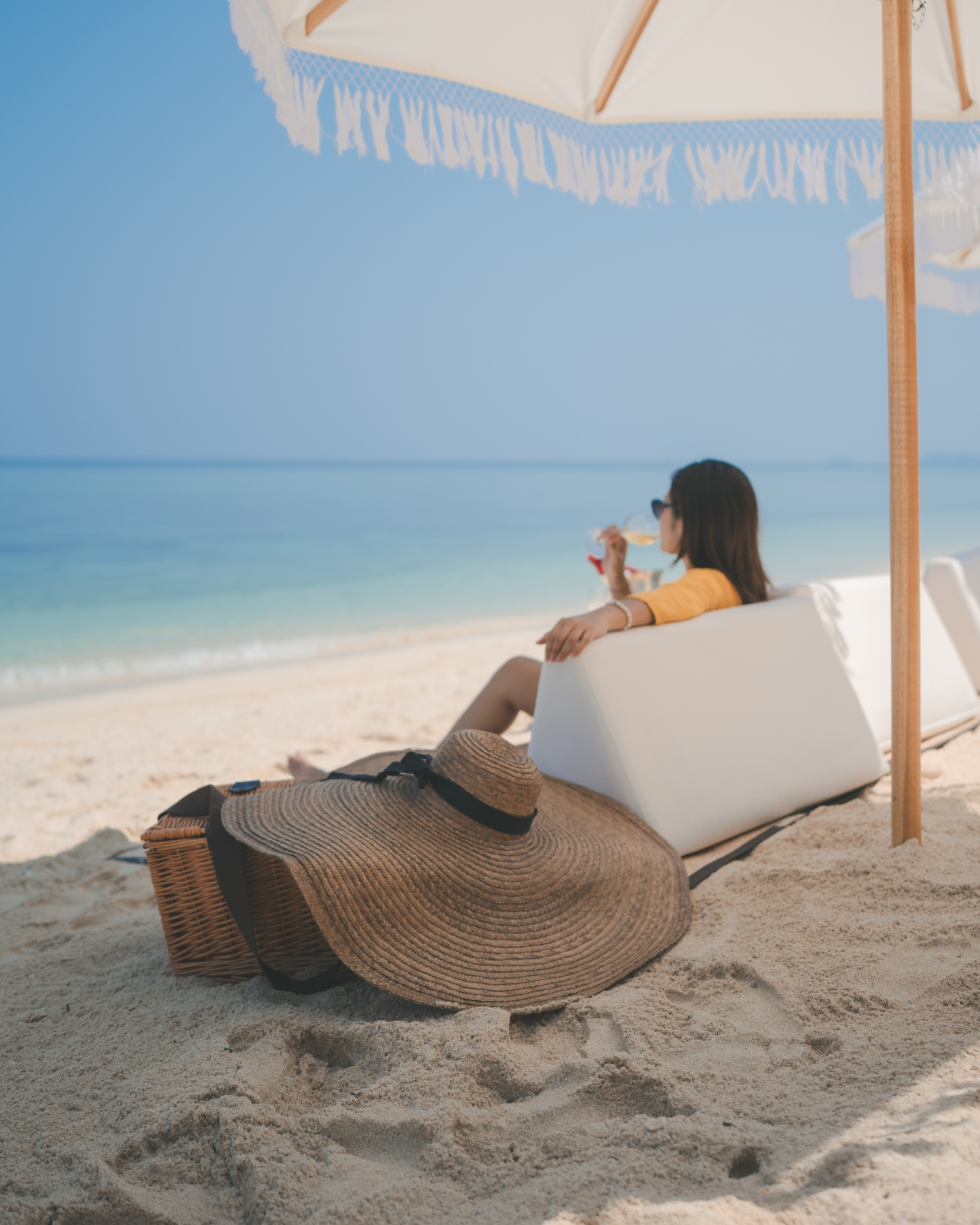 Guest sipping wine on a beach lounger looking out to turquoise water from Mischief's shoreline set-up