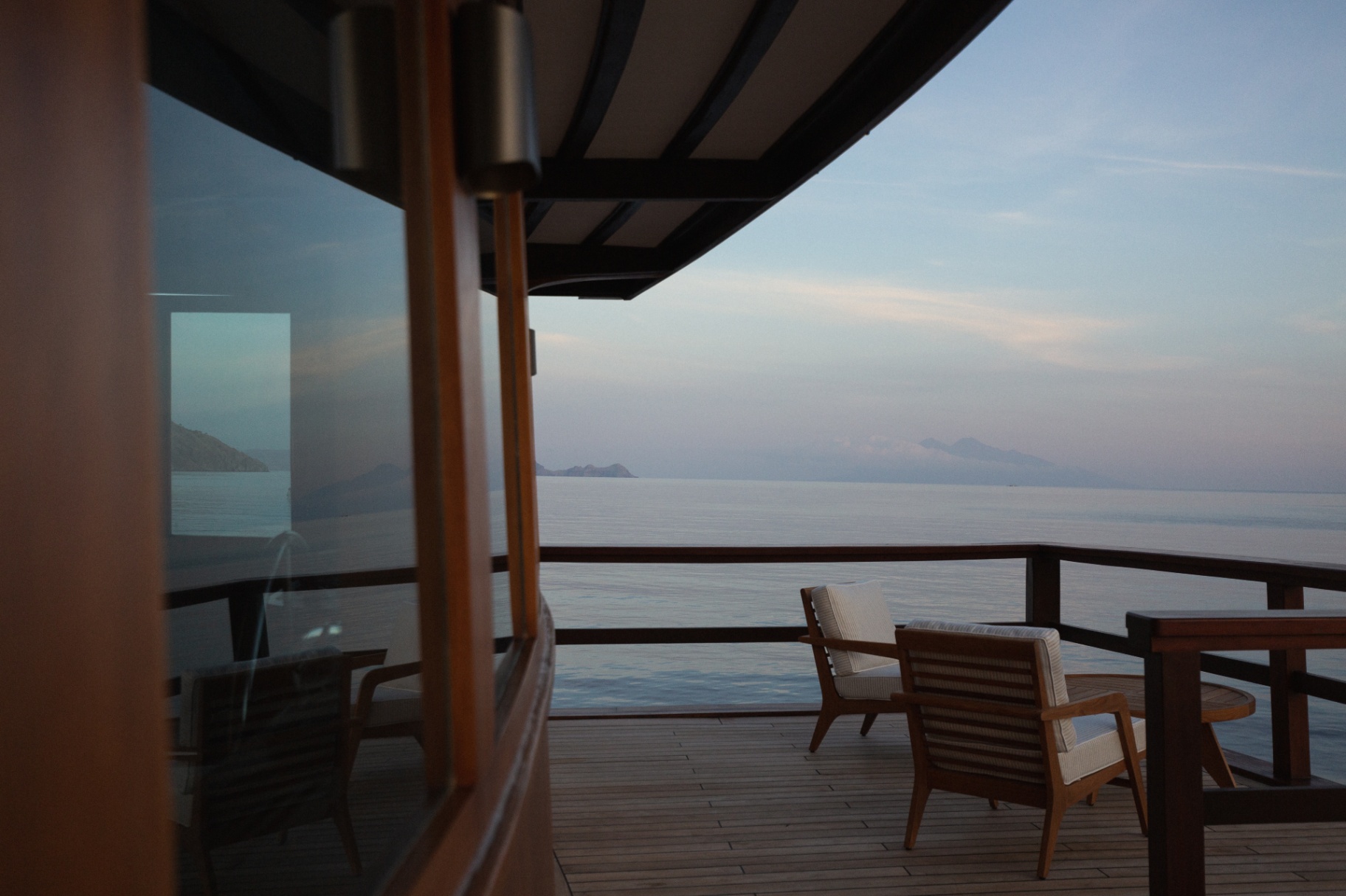 Bridge deck teak terrace with lounge chairs looking out to a calm sea at dusk