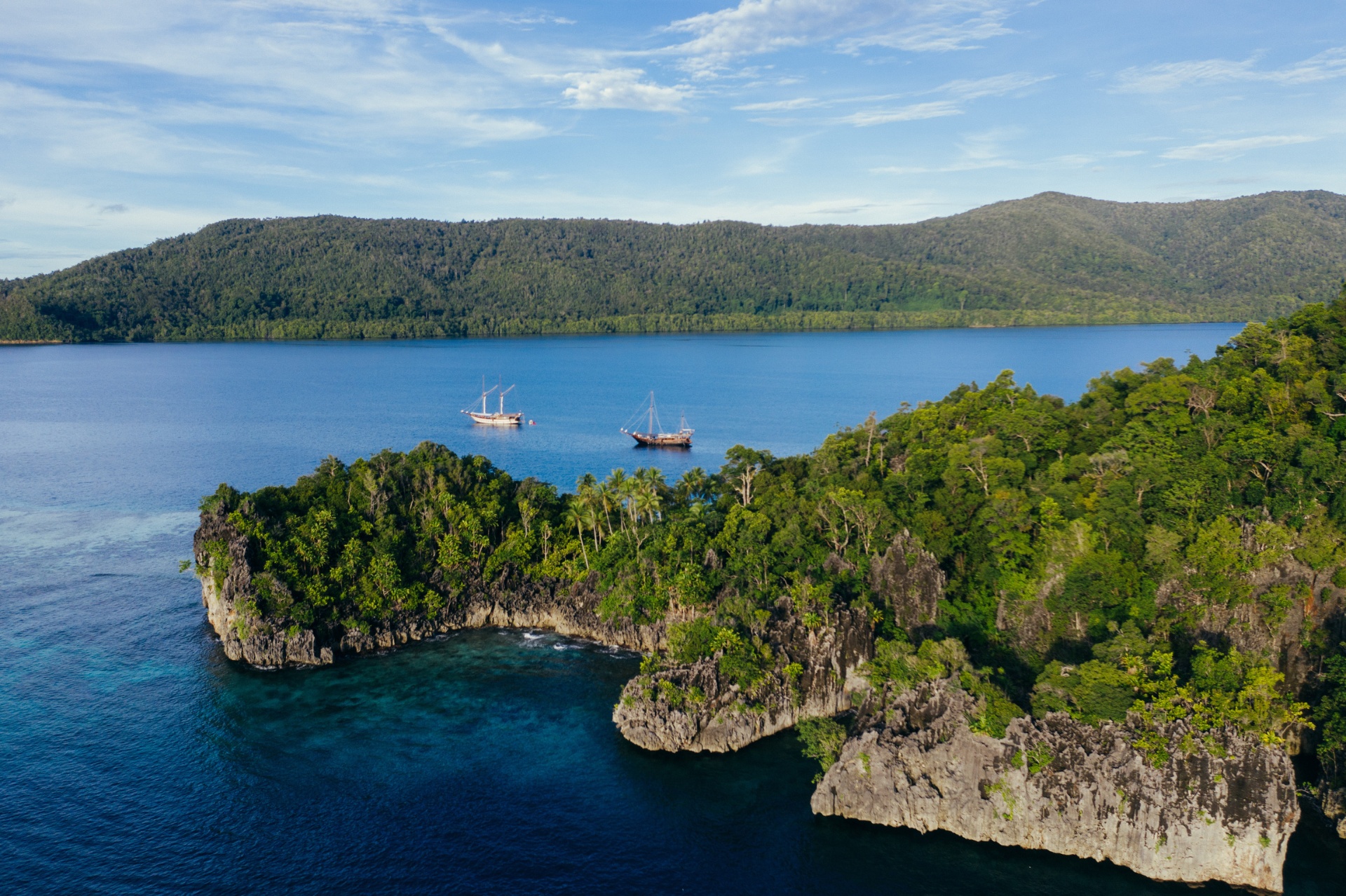 Aerial of Senja and a sister phinisi anchored between karst cliffs and turquoise water in Raja Ampat