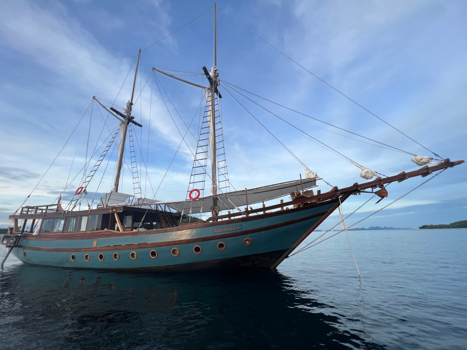Bow-on view of Dewata phinisi anchored in glassy water beside karst islands