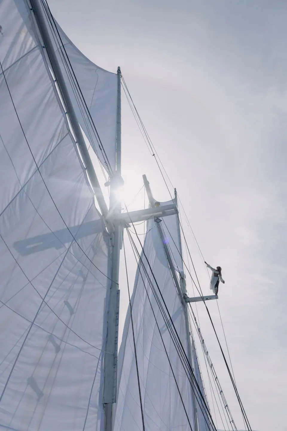Guest standing on Anne Bonny's rigging between full white sails