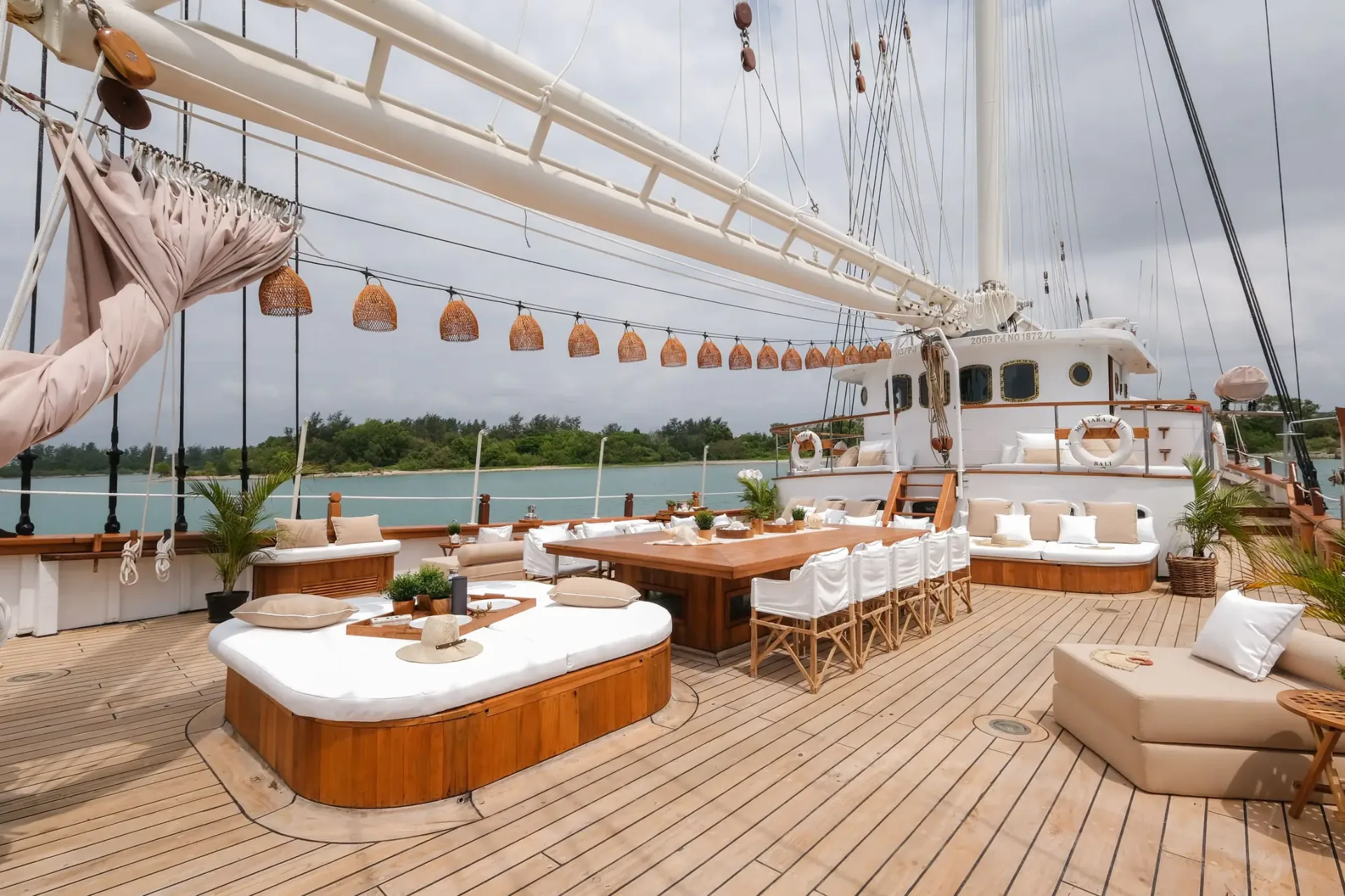 Mutiara Laut main deck with long dining table, daybeds and rigging under open sky