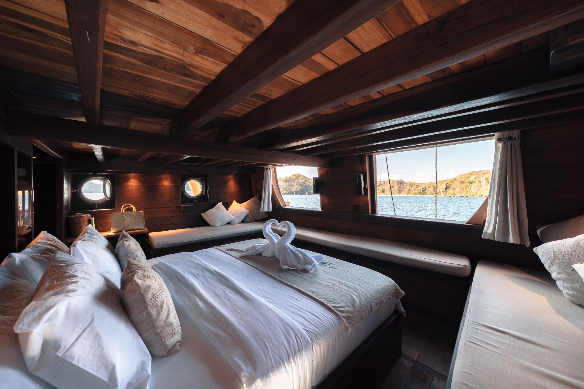 Master cabin on Nataraja with king bed, panoramic windows to green islands and a wooden beam ceiling