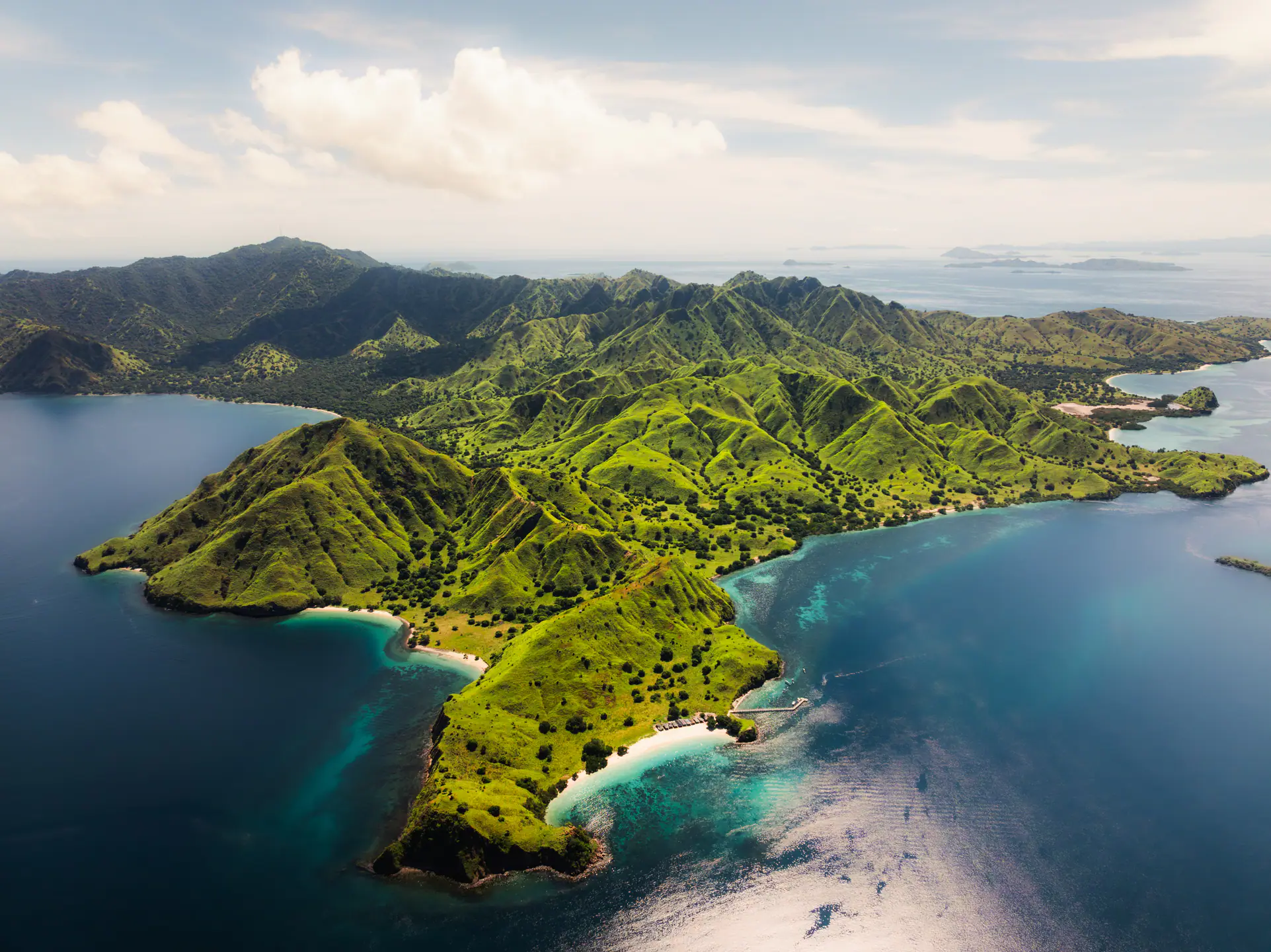 Aerial of Komodo National Park's green ridges meeting turquoise bays and white beaches