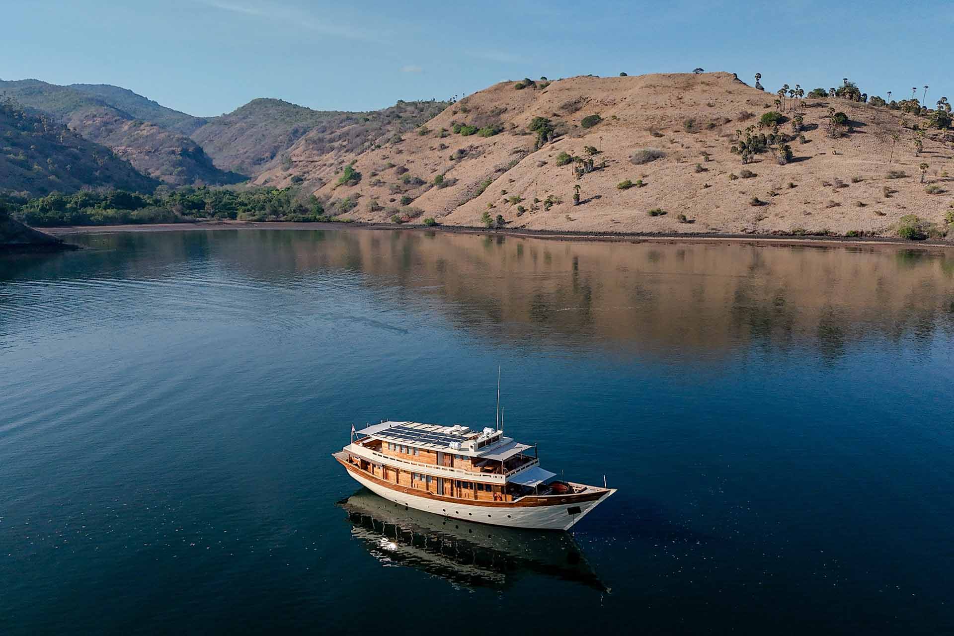 Mischief mirrored on still water in a Komodo bay with dry savannah hills behind