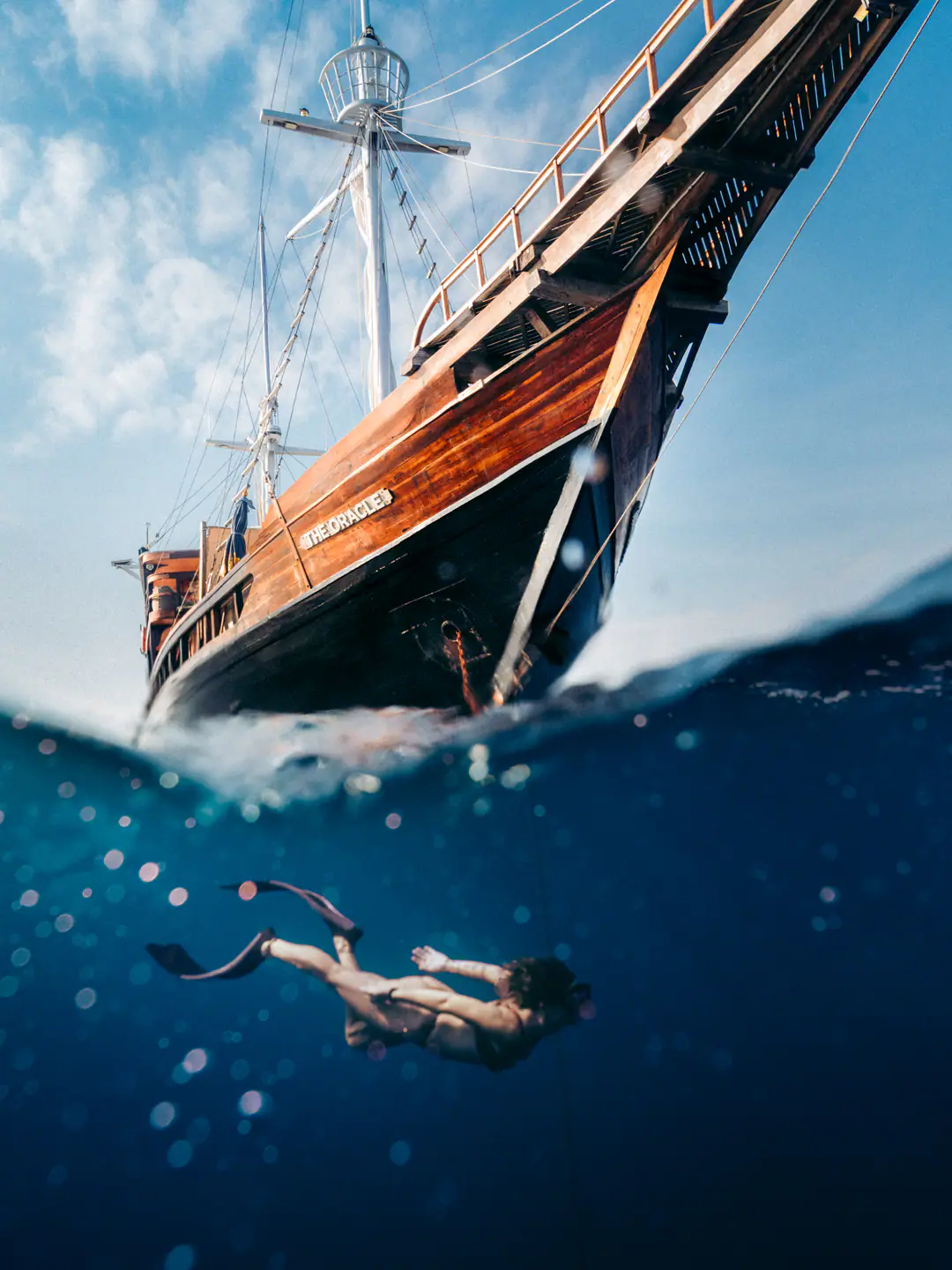 Split view of The Oracle's bow above water with a freediver descending below