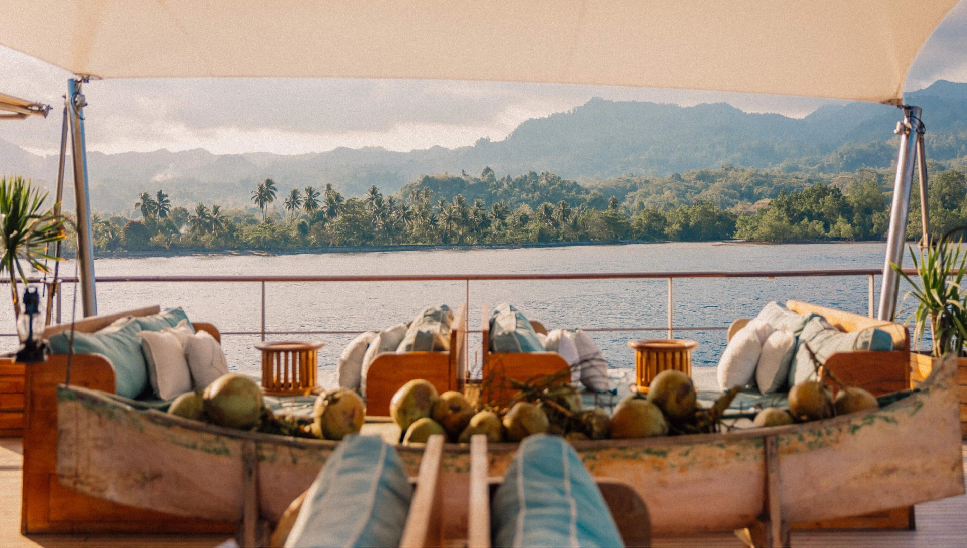 Bow lounge with cushioned banquettes and coconuts, jungle coastline in the distance