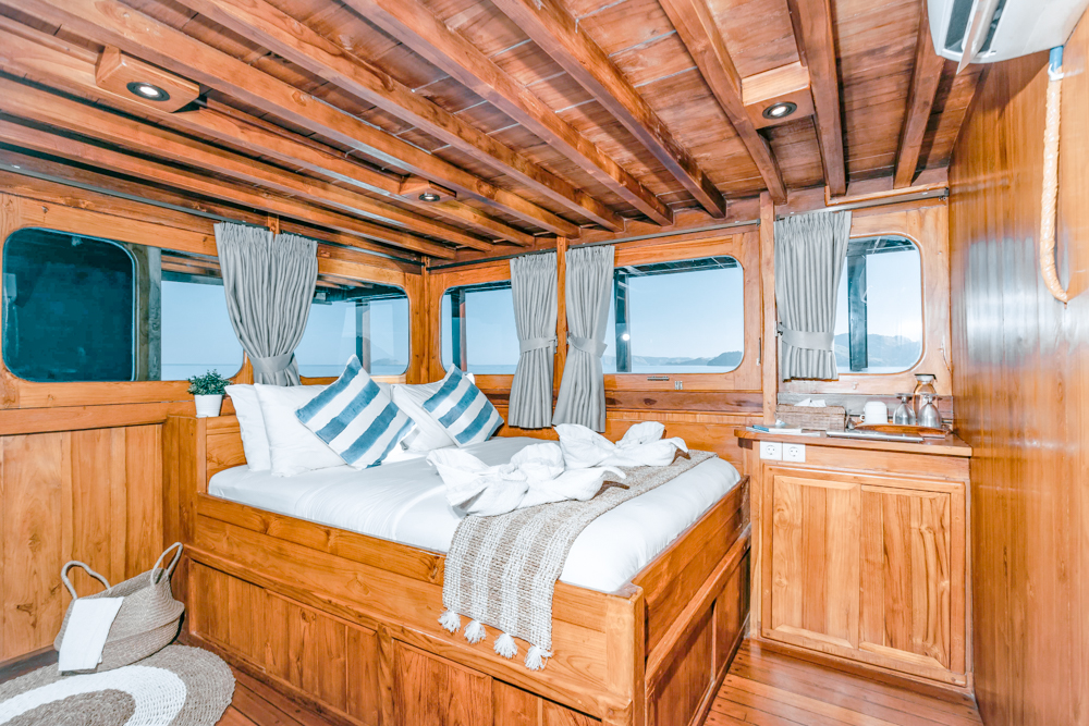Master cabin on Adishree with a wide bed, striped cushions and panoramic windows on both sides