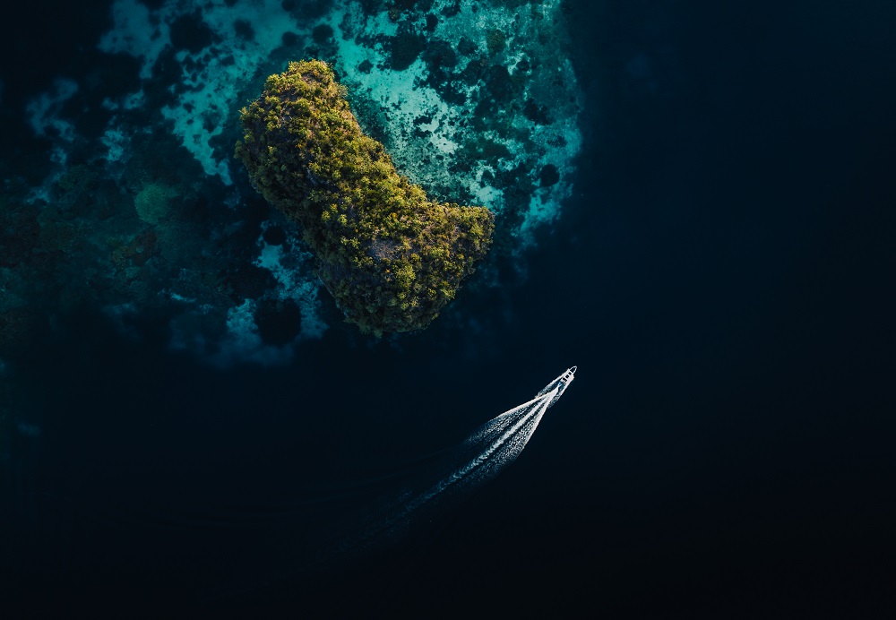 Aerial of Senja's tender speeding past a small coral-fringed islet in Raja Ampat
