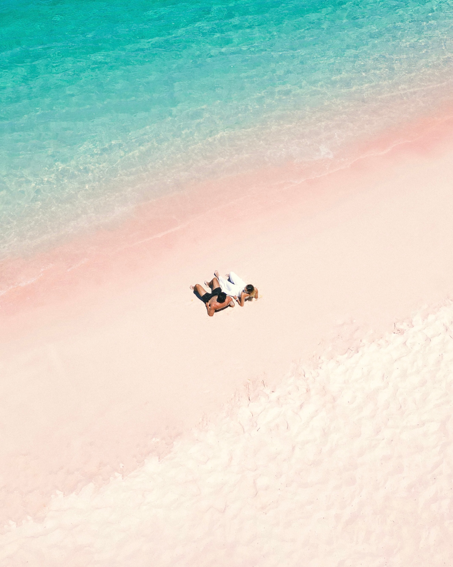 Aerial view of two Mischief guests relaxing on Komodo's famous Pink Beach where turquoise water meets rose-coloured sand
