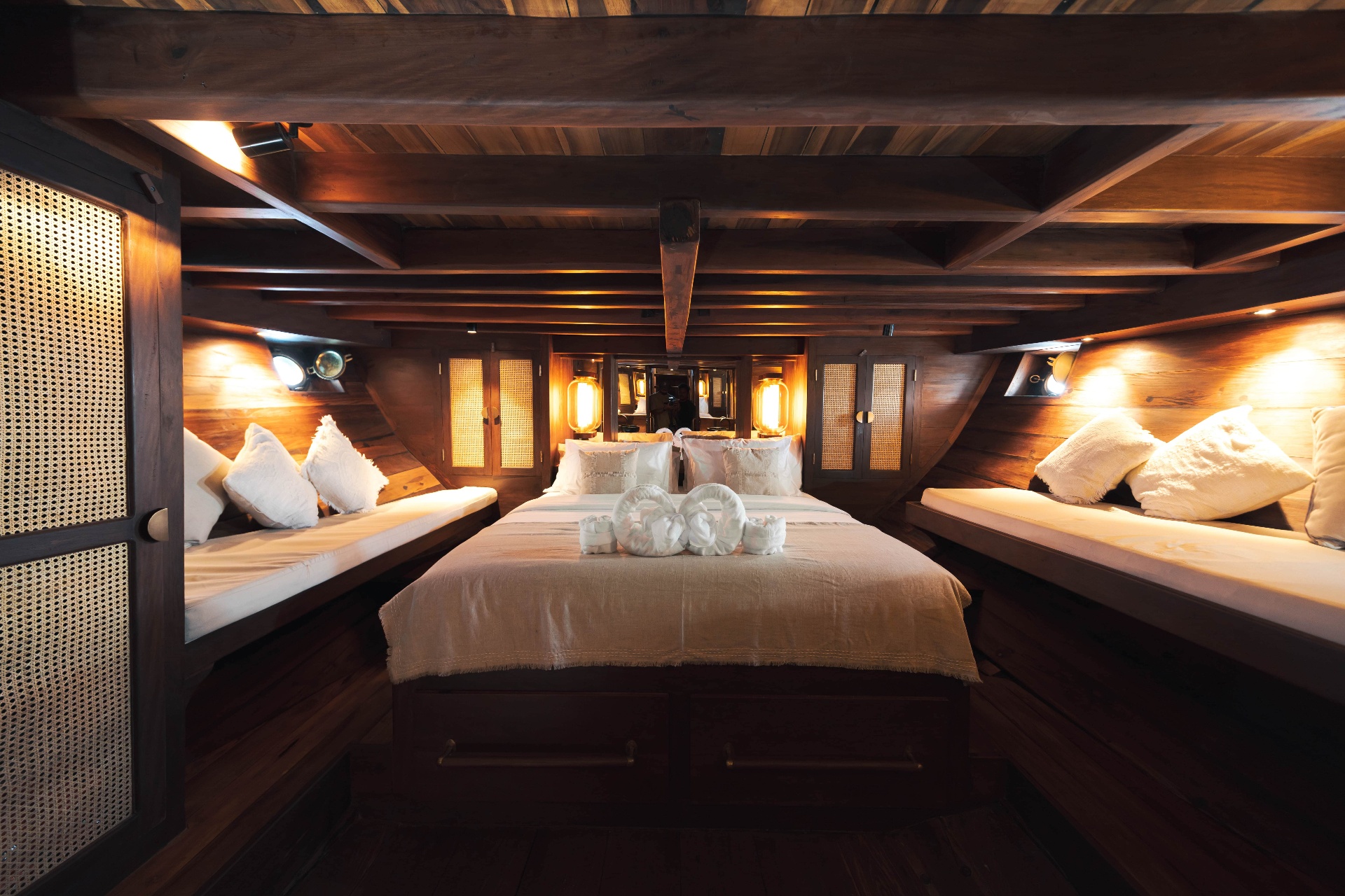 Front cabin on Nataraja with king bed, side benches and cane wardrobes under a beamed ceiling