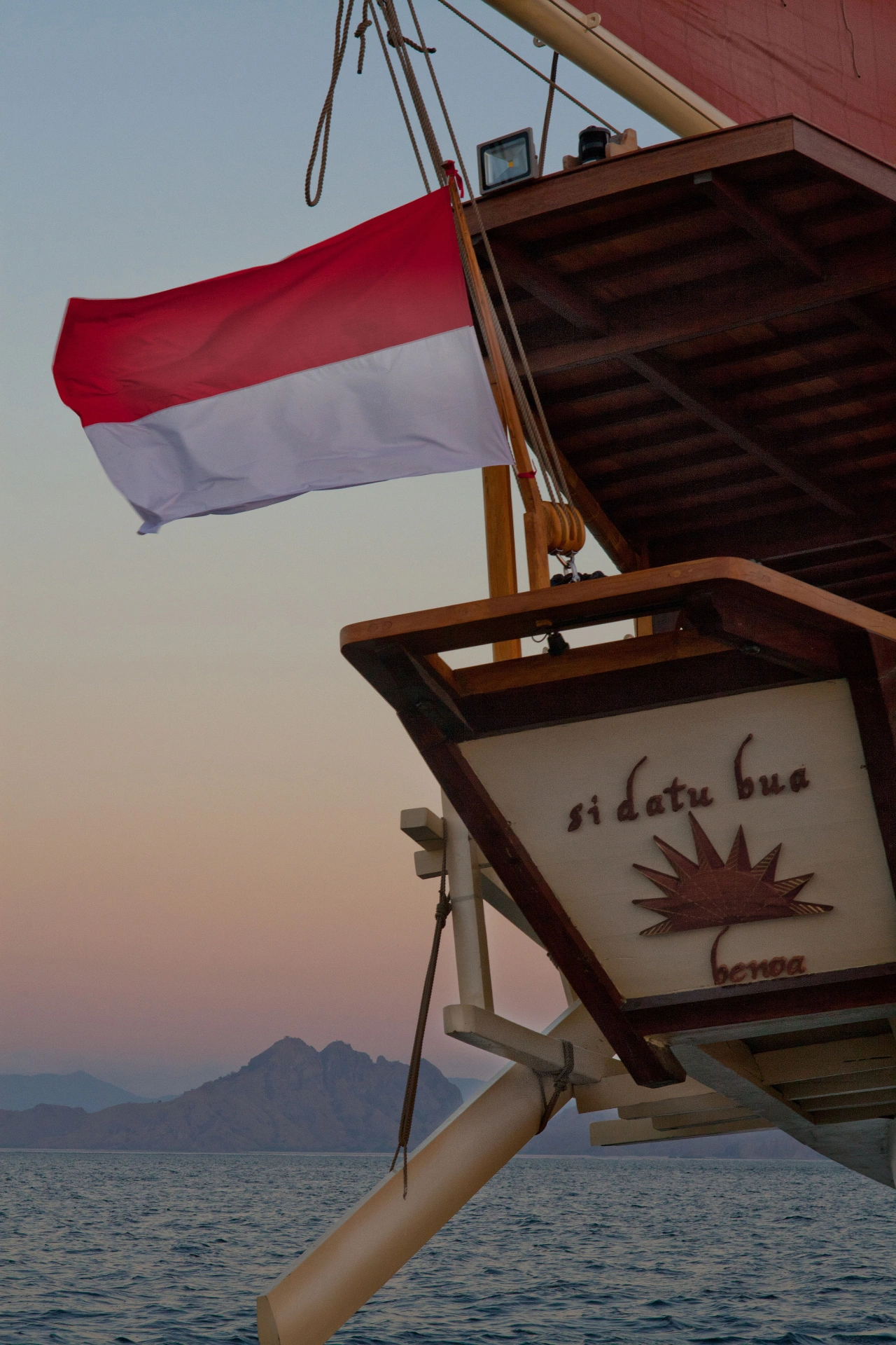 Si Datu Bua stern nameboard with the Indonesian flag flying at dusk off Komodo