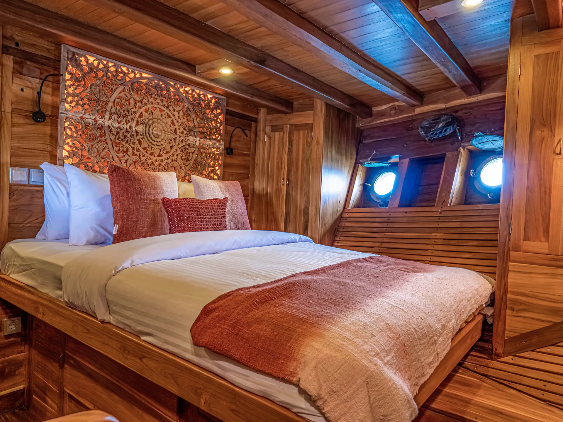 Master cabin on Anne Bonny with carved teak headboard and porthole windows