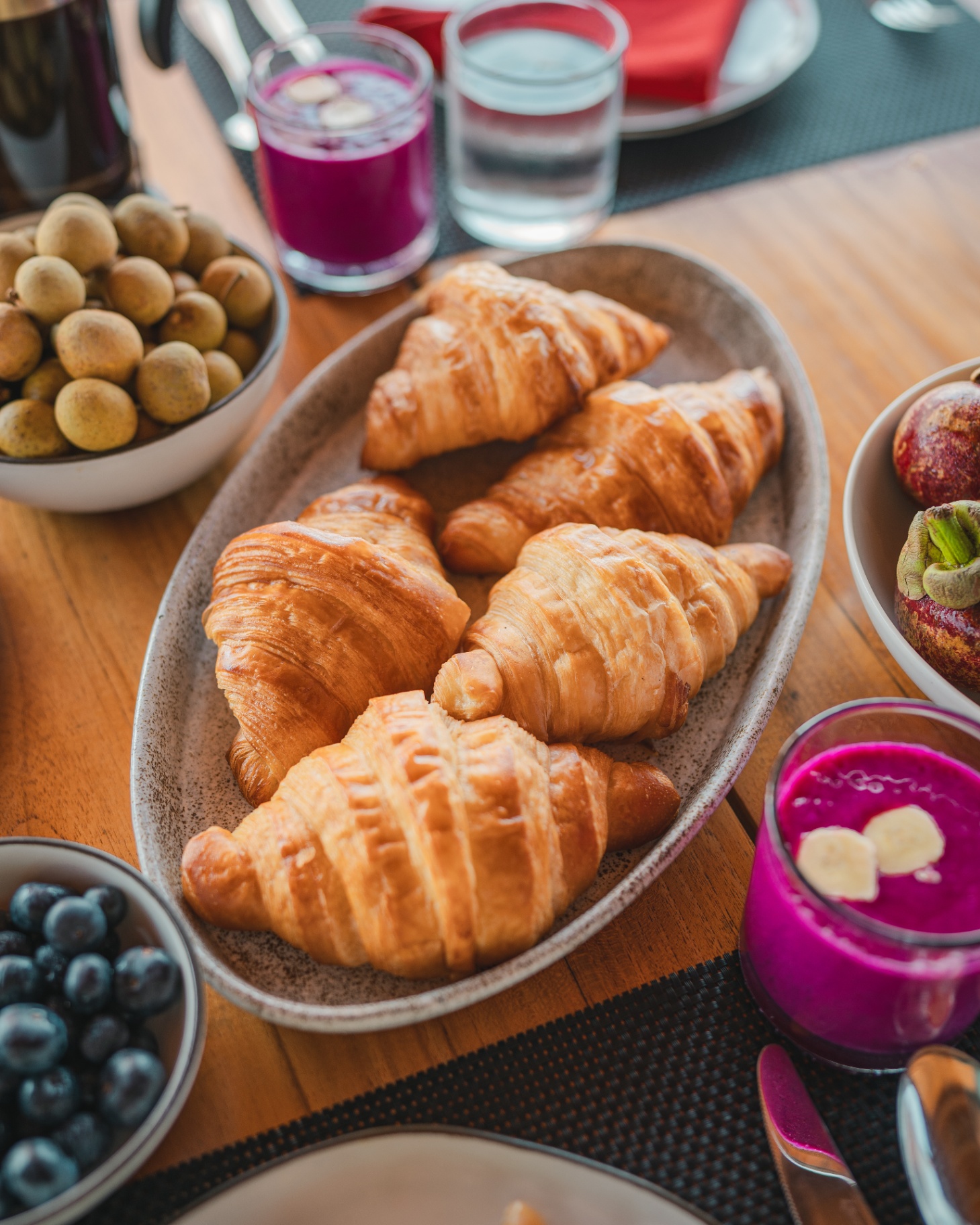 Breakfast spread on Mischief with fresh croissants, dragon fruit smoothie, longan, mangosteen and blueberries