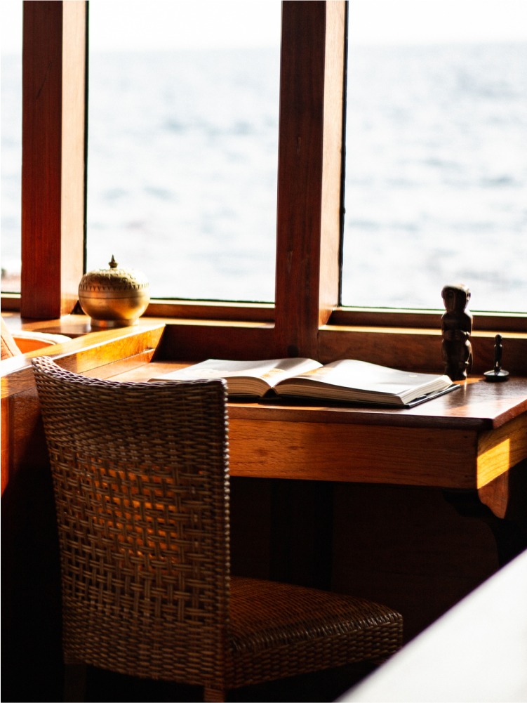 Writing desk with open book and small carving beside a picture window looking out to sea on Si Datu Bua