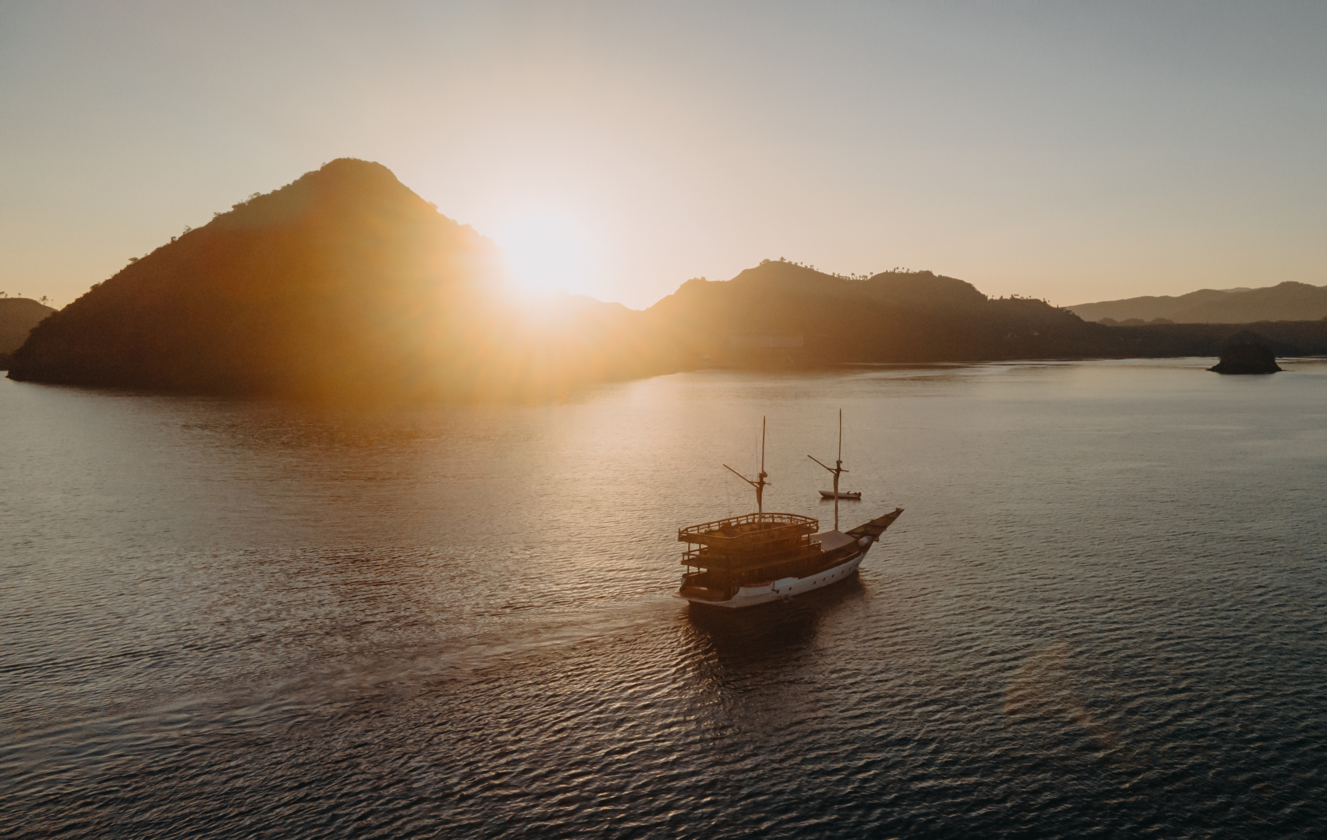 Andamari silhouetted against a golden sunset behind Komodo hills on calm water