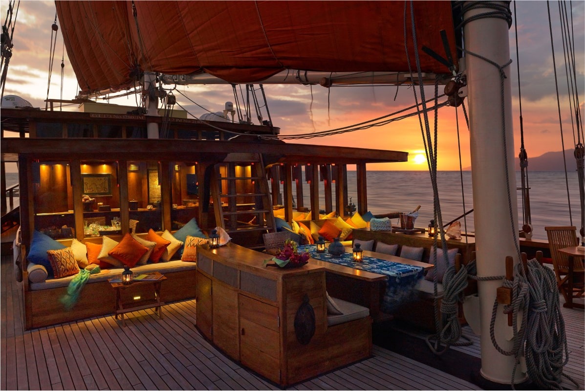 Aft-deck lounge on Si Datu Bua at sunset with lanterns, colourful ikat cushions and cocktail service