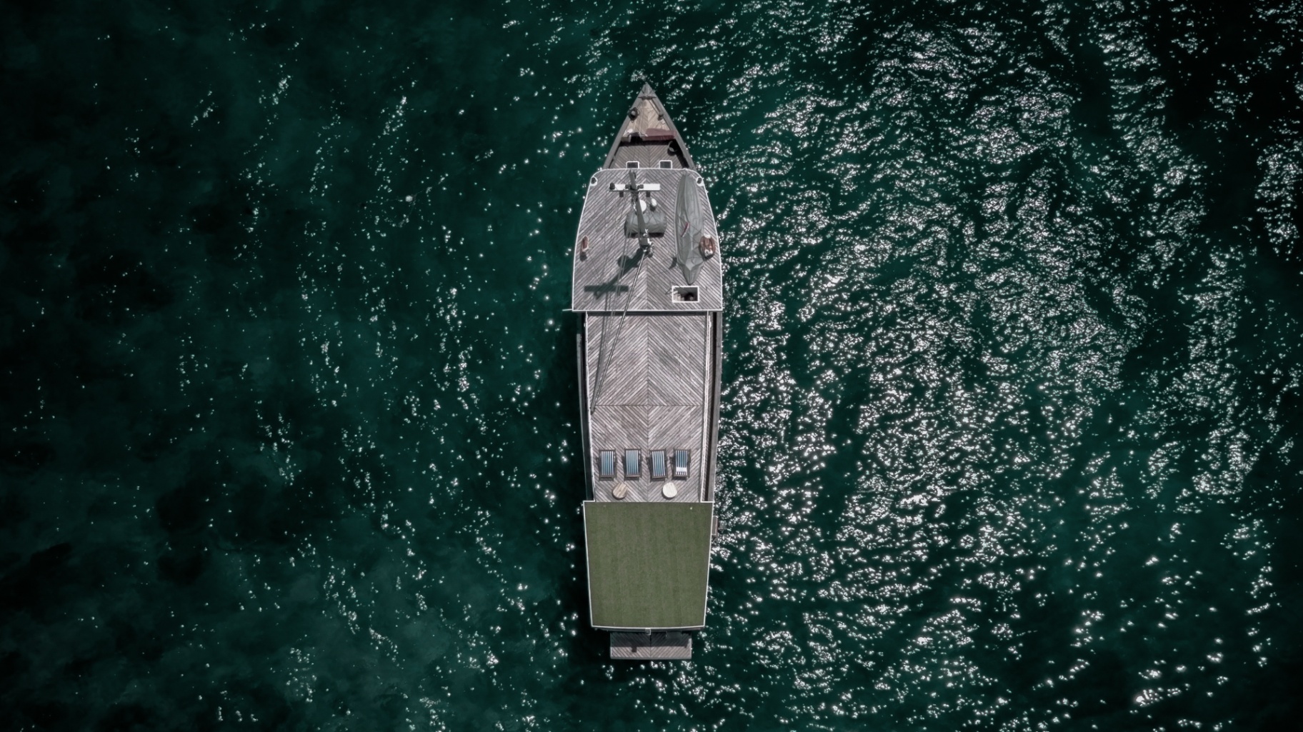 Aerial top-down view of Splendour phinisi on deep emerald water with sun loungers on the aft deck