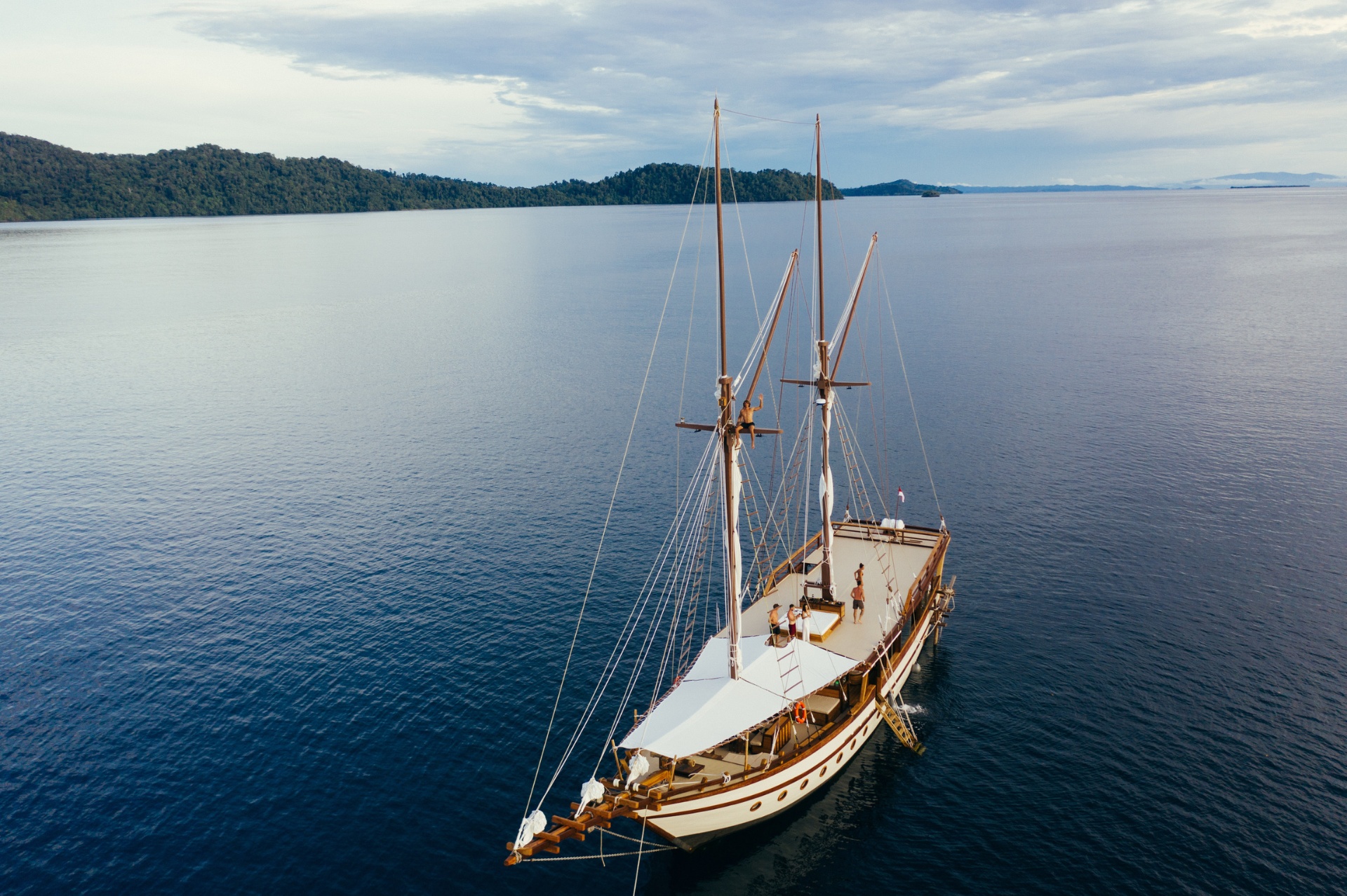 Crew member climbing Senja's mast while guests relax on the sundeck