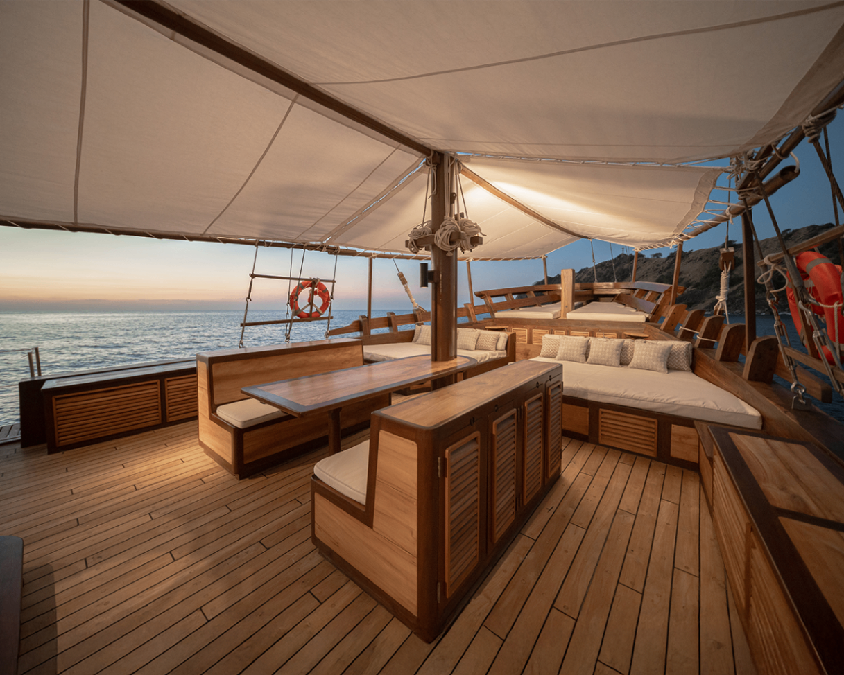 Sanya's foredeck lounge at dusk with shaded seating, daybeds and teak dining table