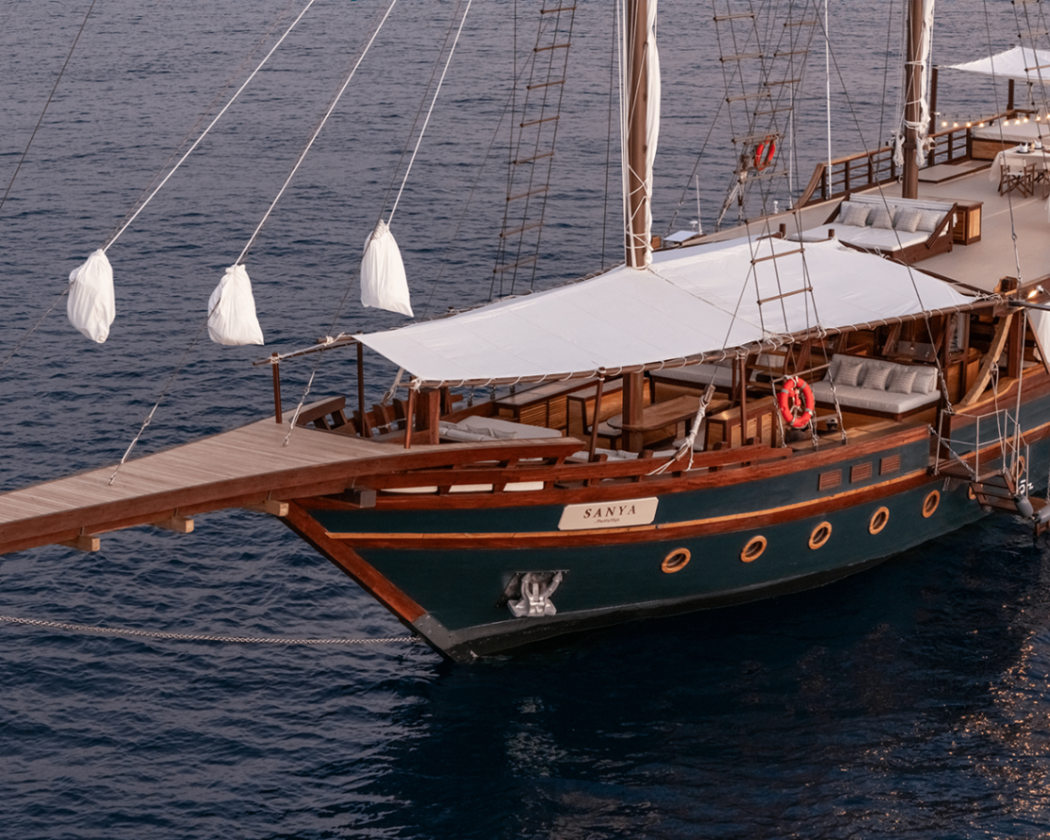 Close-up of Sanya's bow and foredeck lounge at dusk with teak details and sea beyond