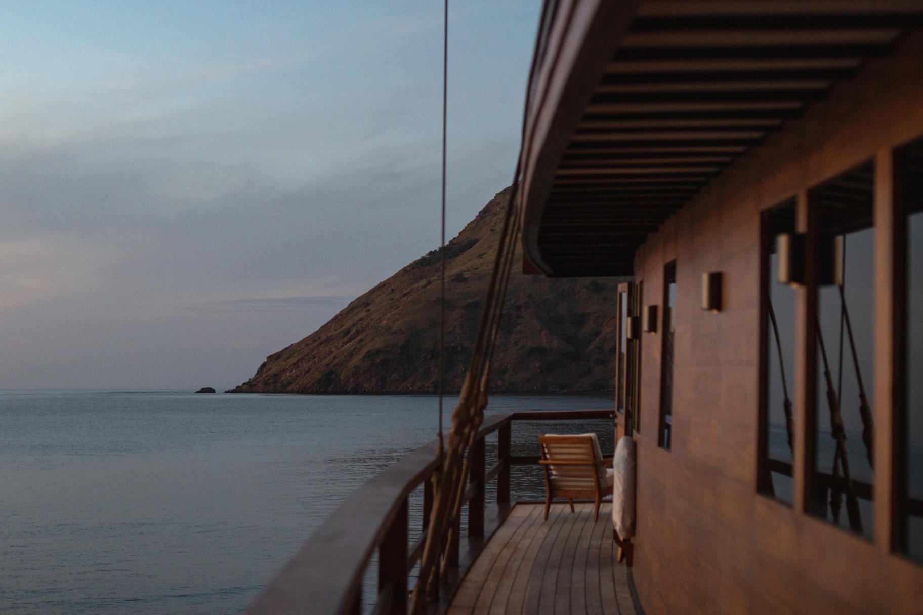 Vela's teak side deck at dusk with a single chair and view of a Komodo hillside