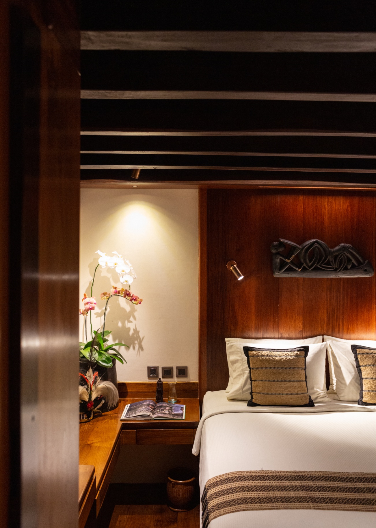 Cabin bedside on Silolona with orchid, guidebook and carved Asmat headboard sculpture